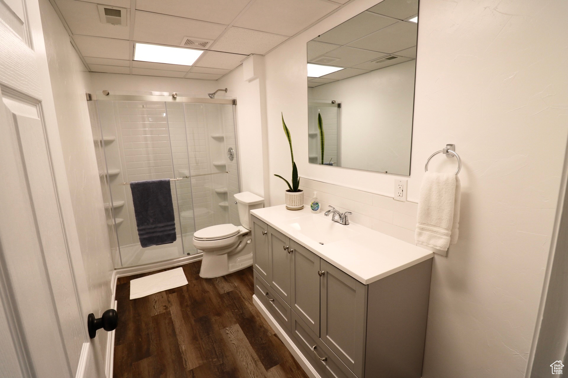 Bathroom featuring hardwood / wood-style flooring, toilet, a drop ceiling, walk in shower, and vanity