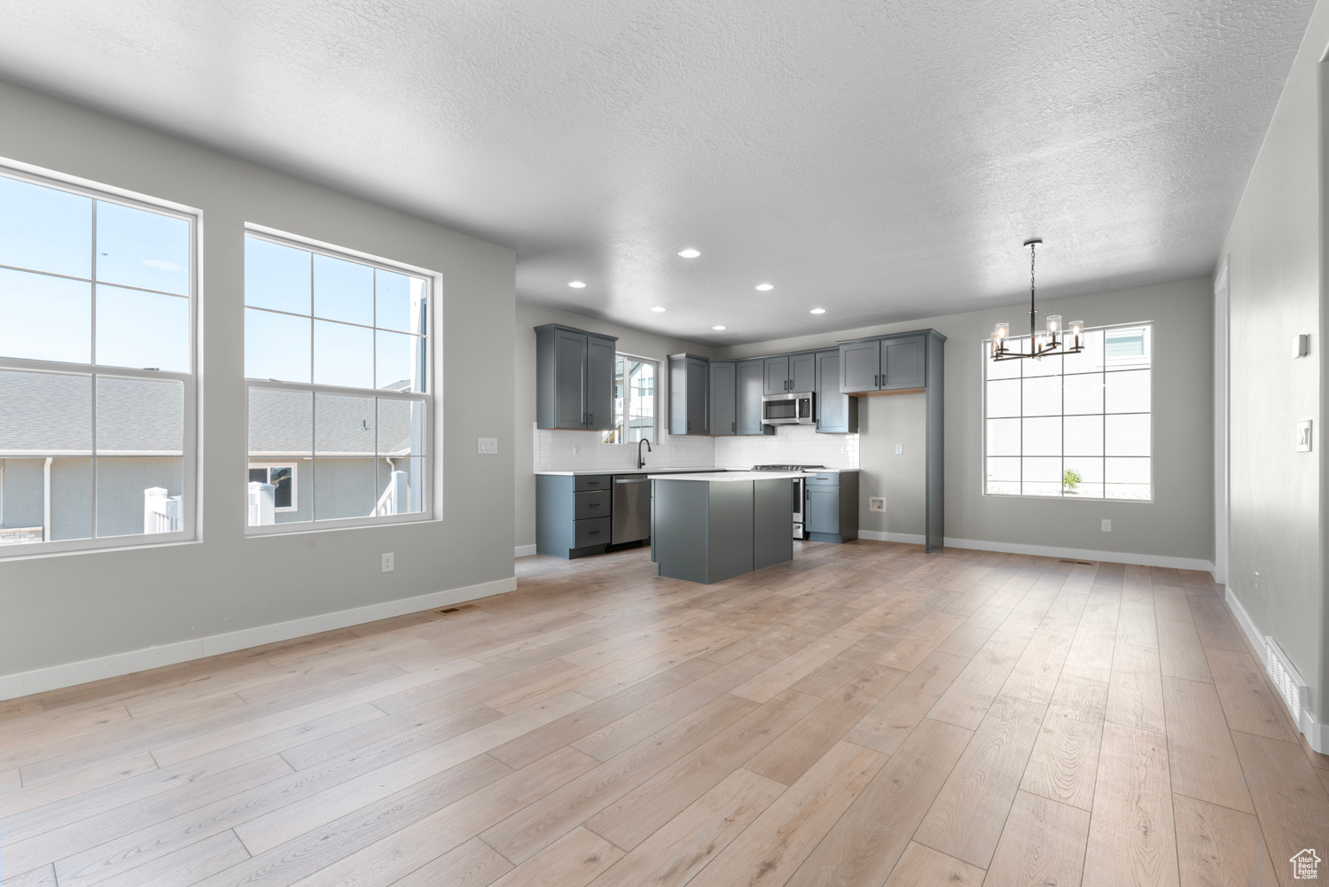 Unfurnished living room featuring light hardwood / wood-style floors, sink, a textured ceiling, and a chandelier