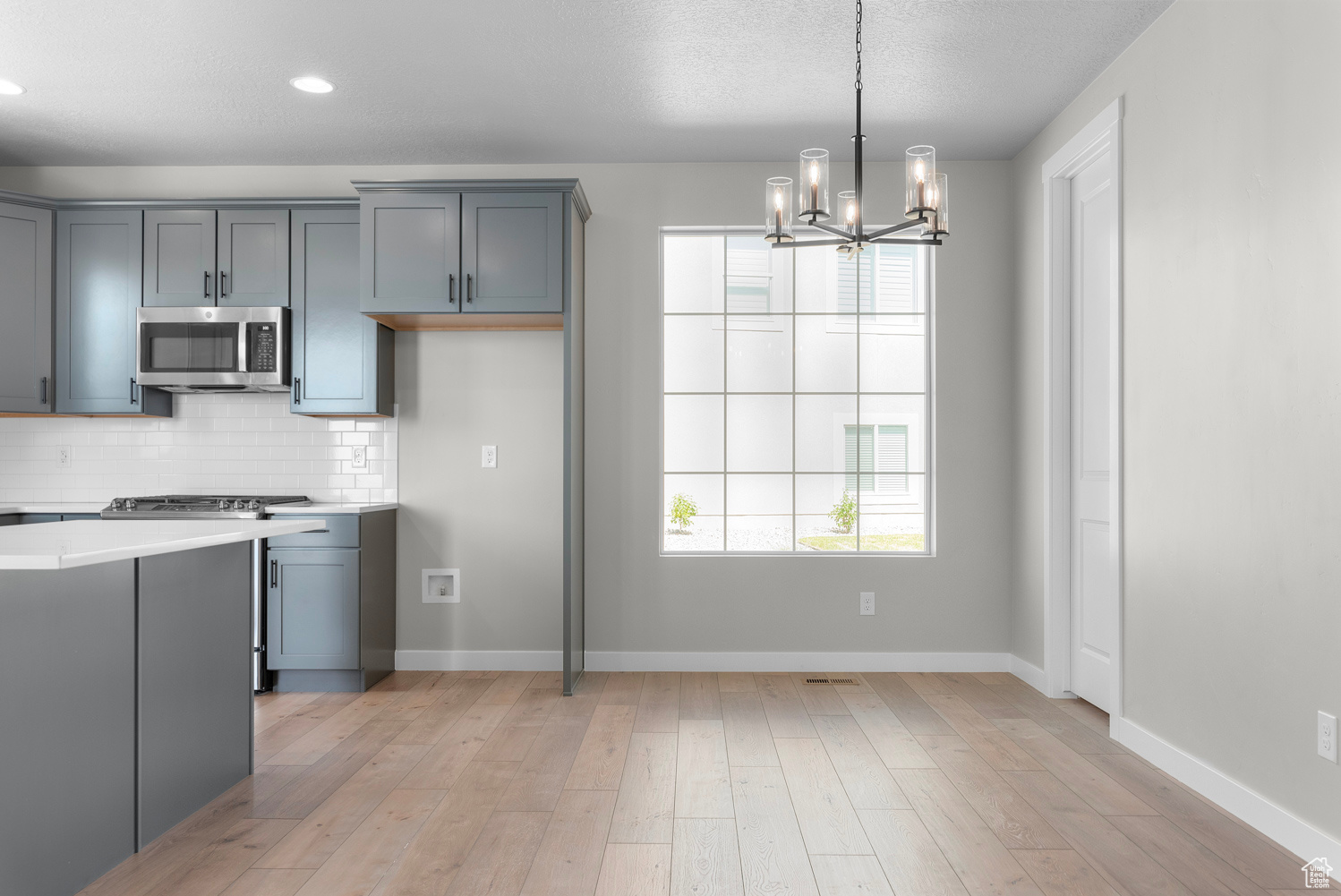 Kitchen with backsplash, light hardwood / wood-style floors, stove, and gray cabinetry