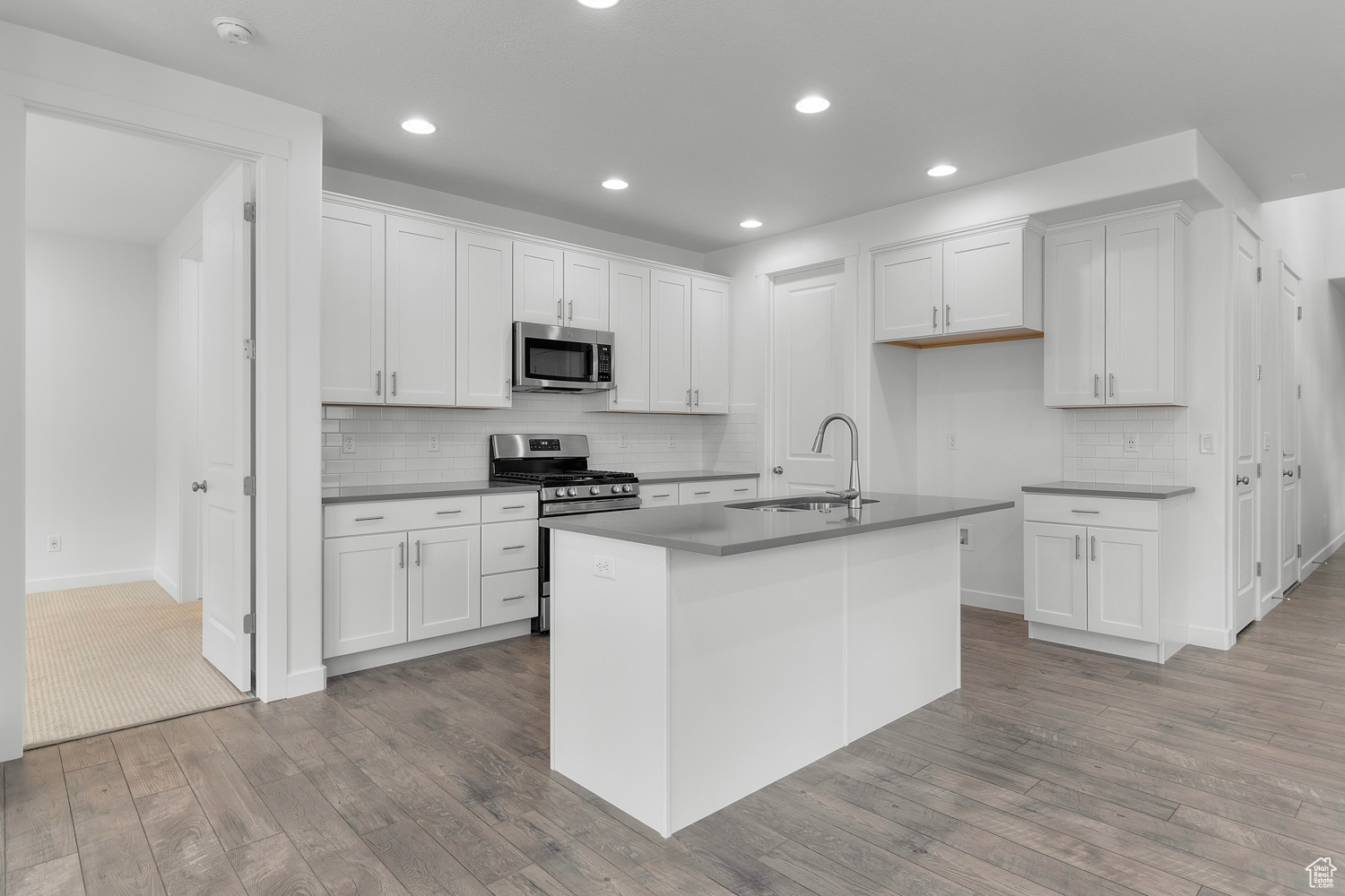 Kitchen with stainless steel appliances, sink, a center island with sink, white cabinets, and light hardwood / wood-style floors