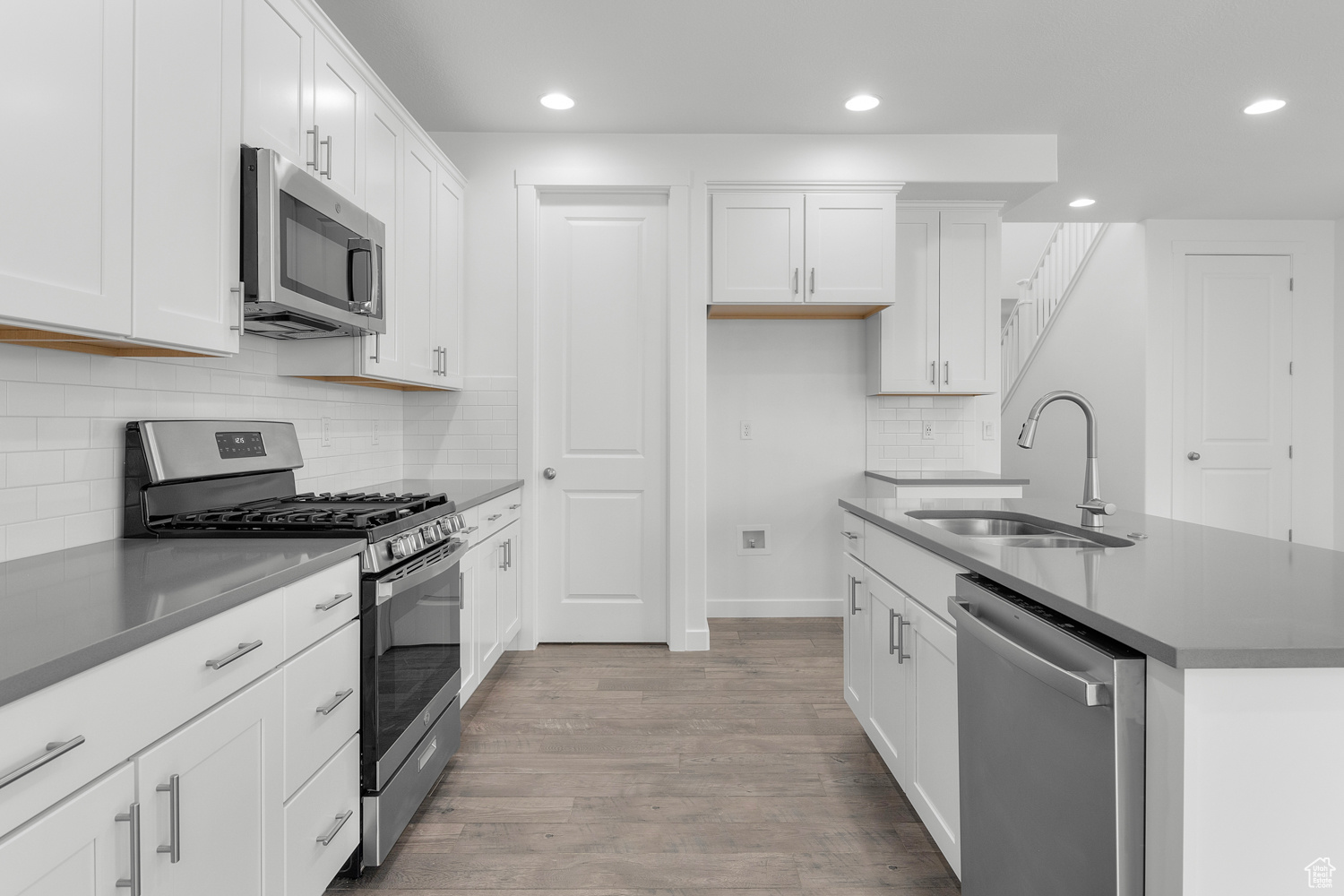 Kitchen with tasteful backsplash, light hardwood / wood-style flooring, stainless steel appliances, sink, and white cabinets