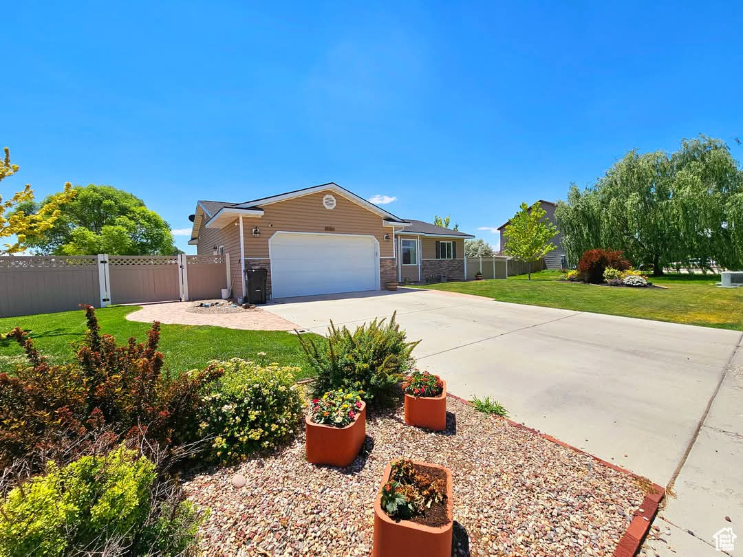 Ranch-style house with a garage, concrete driveway, fence, and a front lawn