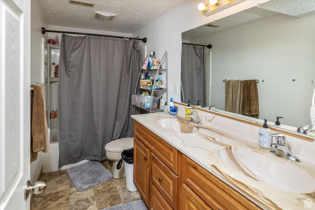 Full bathroom 4 with double vanity, toilet, tile floors, shower/tub combo, and a textured ceiling