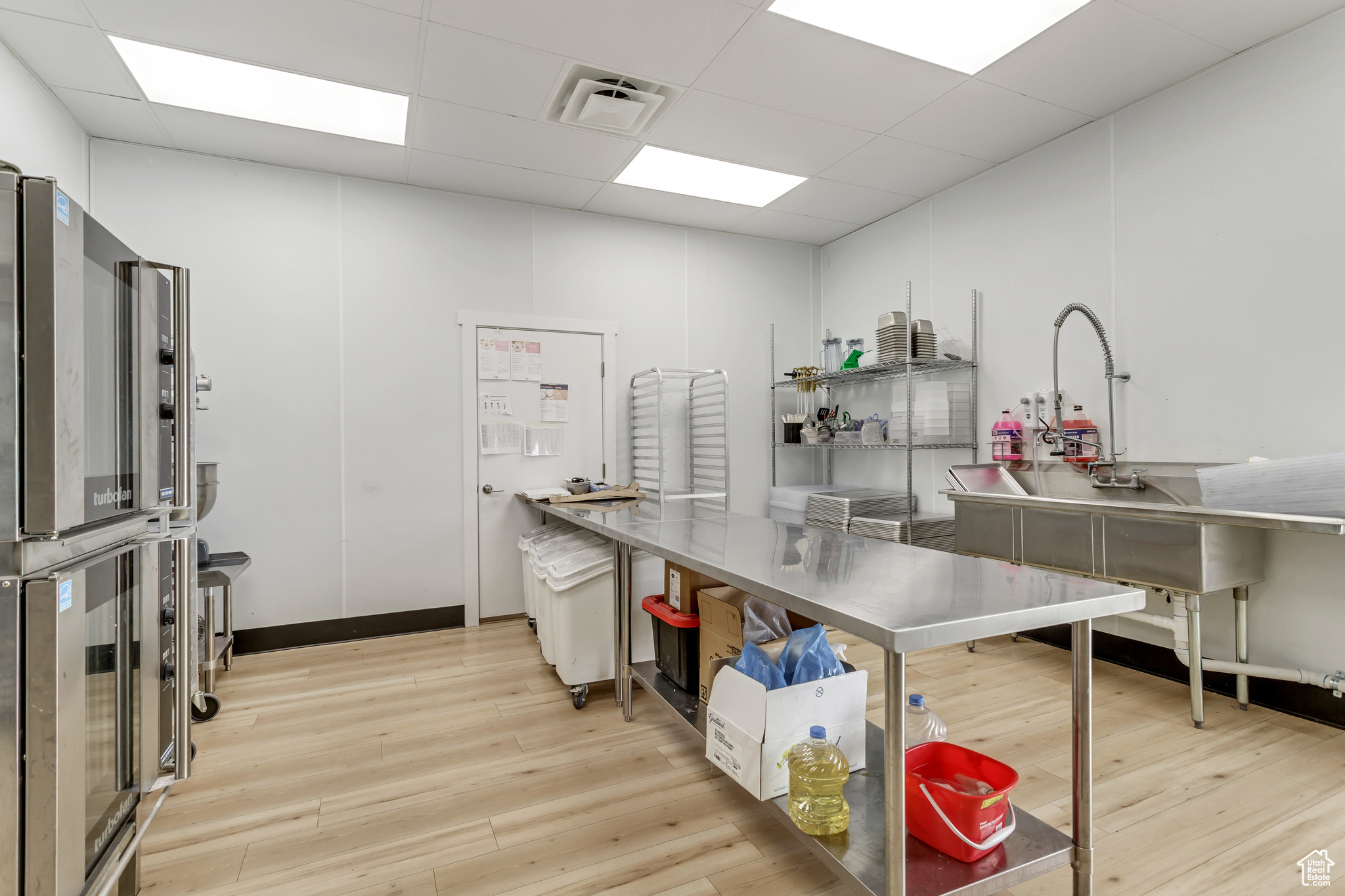 Kitchen with stainless steel counters, light hardwood / wood-style flooring, and a drop ceiling