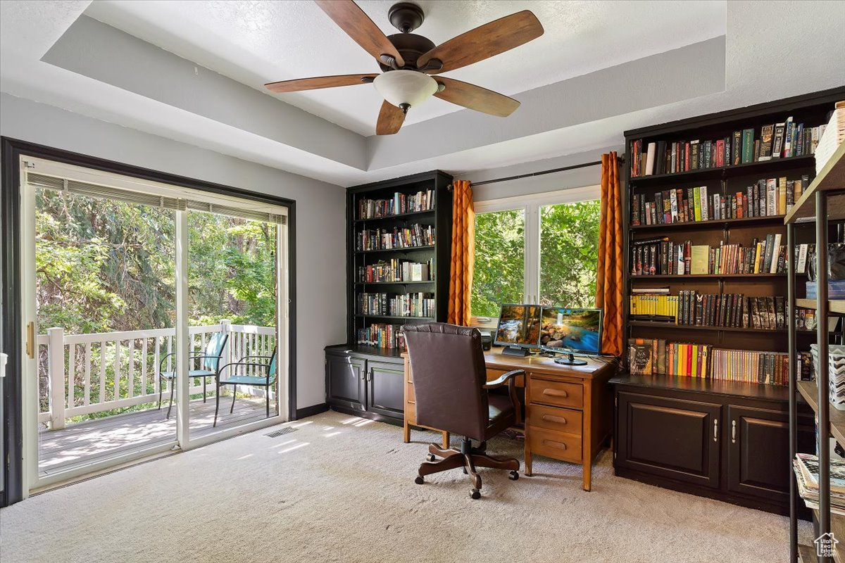 Carpeted office space featuring ceiling fan and a tray ceiling