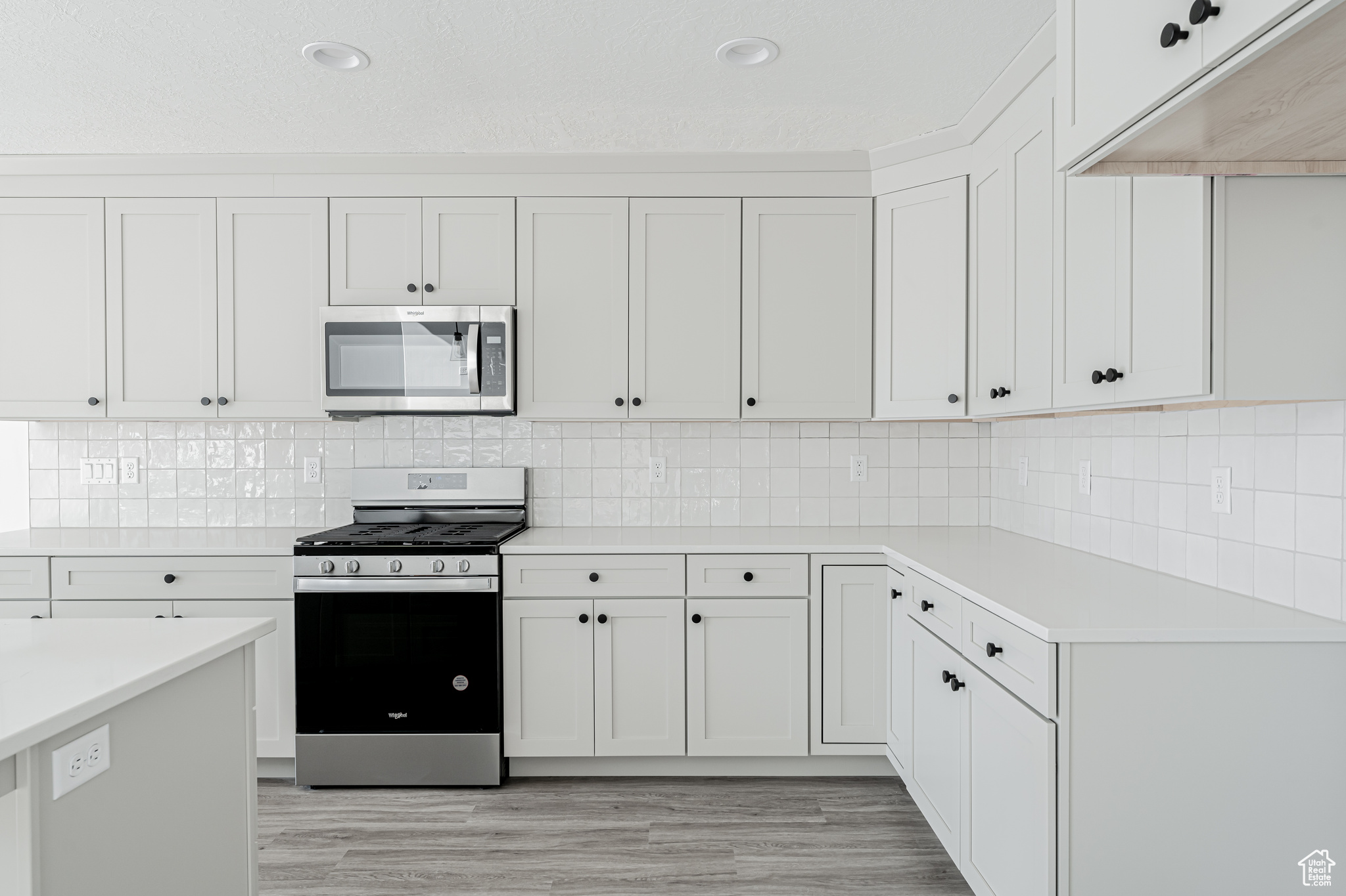 Kitchen with tasteful backsplash, appliances with stainless steel finishes, light hardwood / wood-style flooring, and white cabinets