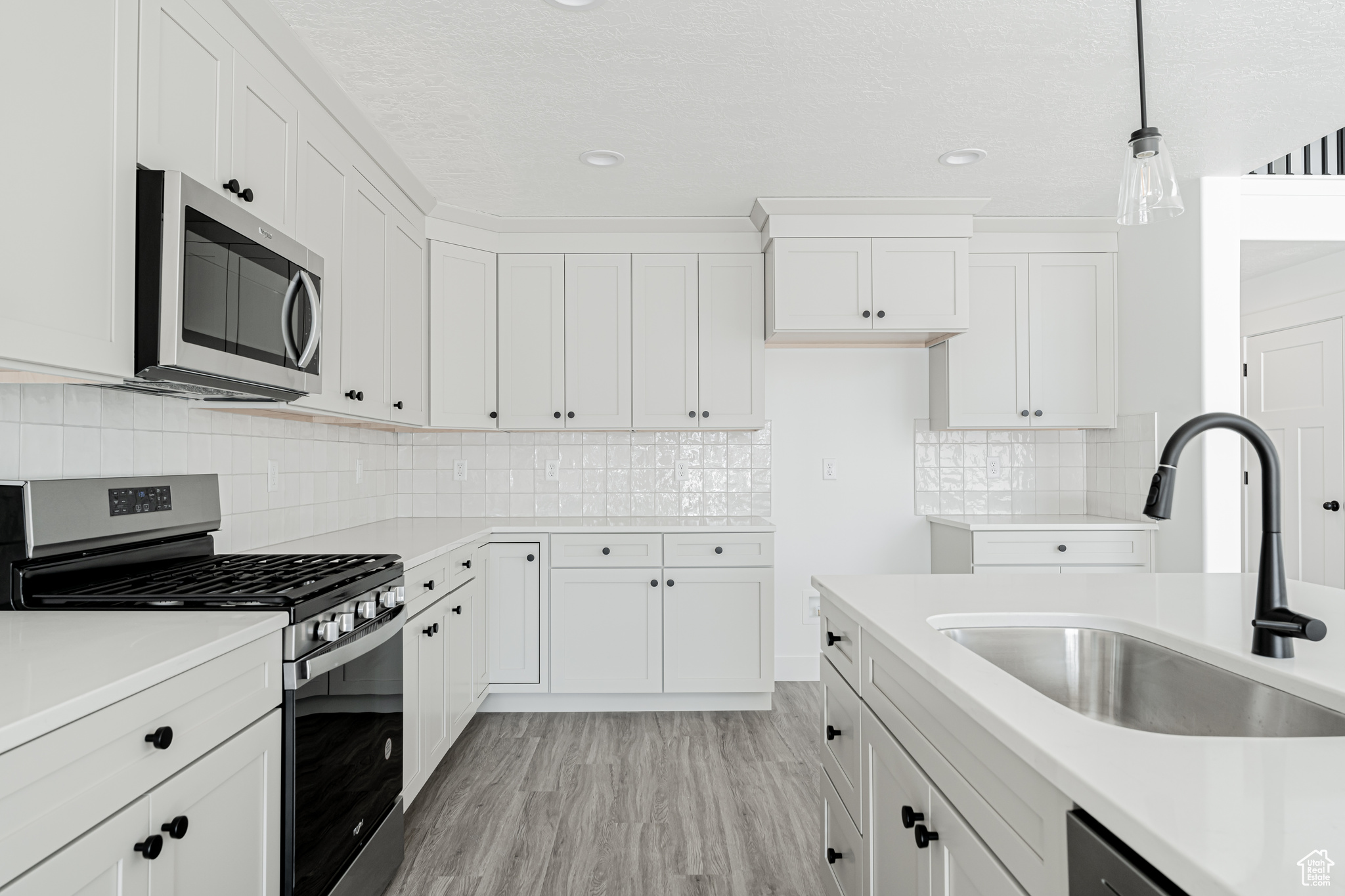 Kitchen with sink, light hardwood / wood-style flooring, white cabinetry, stainless steel appliances, and decorative light fixtures