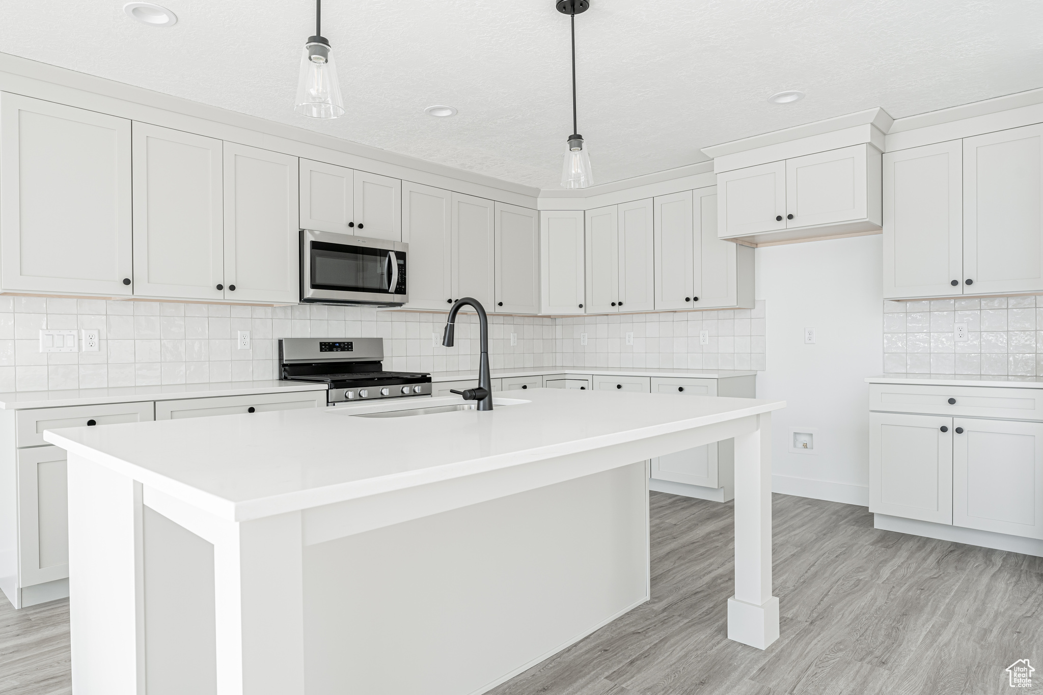 Kitchen featuring stainless steel appliances, a kitchen island with sink, pendant lighting, and white cabinets