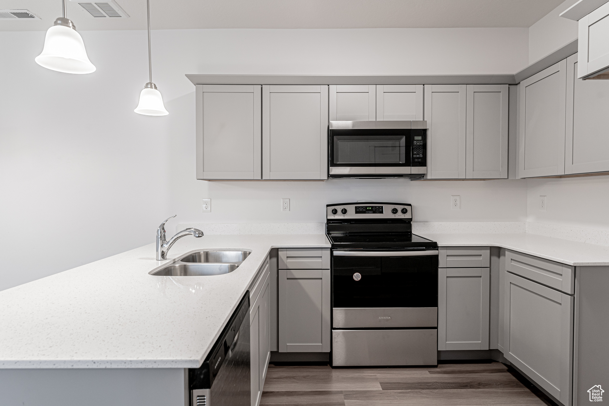 Kitchen featuring gray cabinetry, sink, hanging light fixtures, and appliances with stainless steel finishes