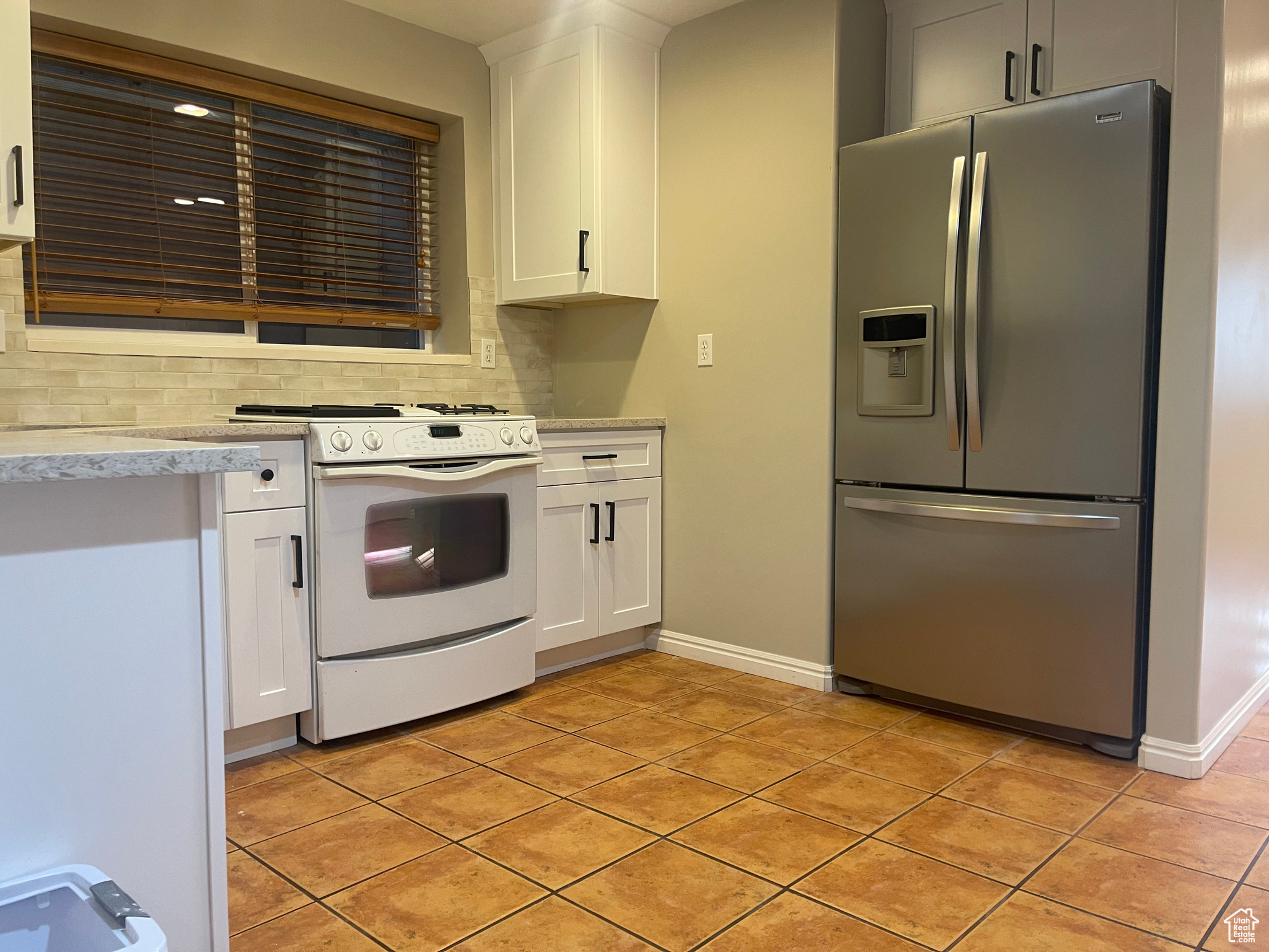 Kitchen with white cabinetry, tasteful backsplash, light tile patterned floors, white gas range oven, and stainless steel refrigerator with ice dispenser