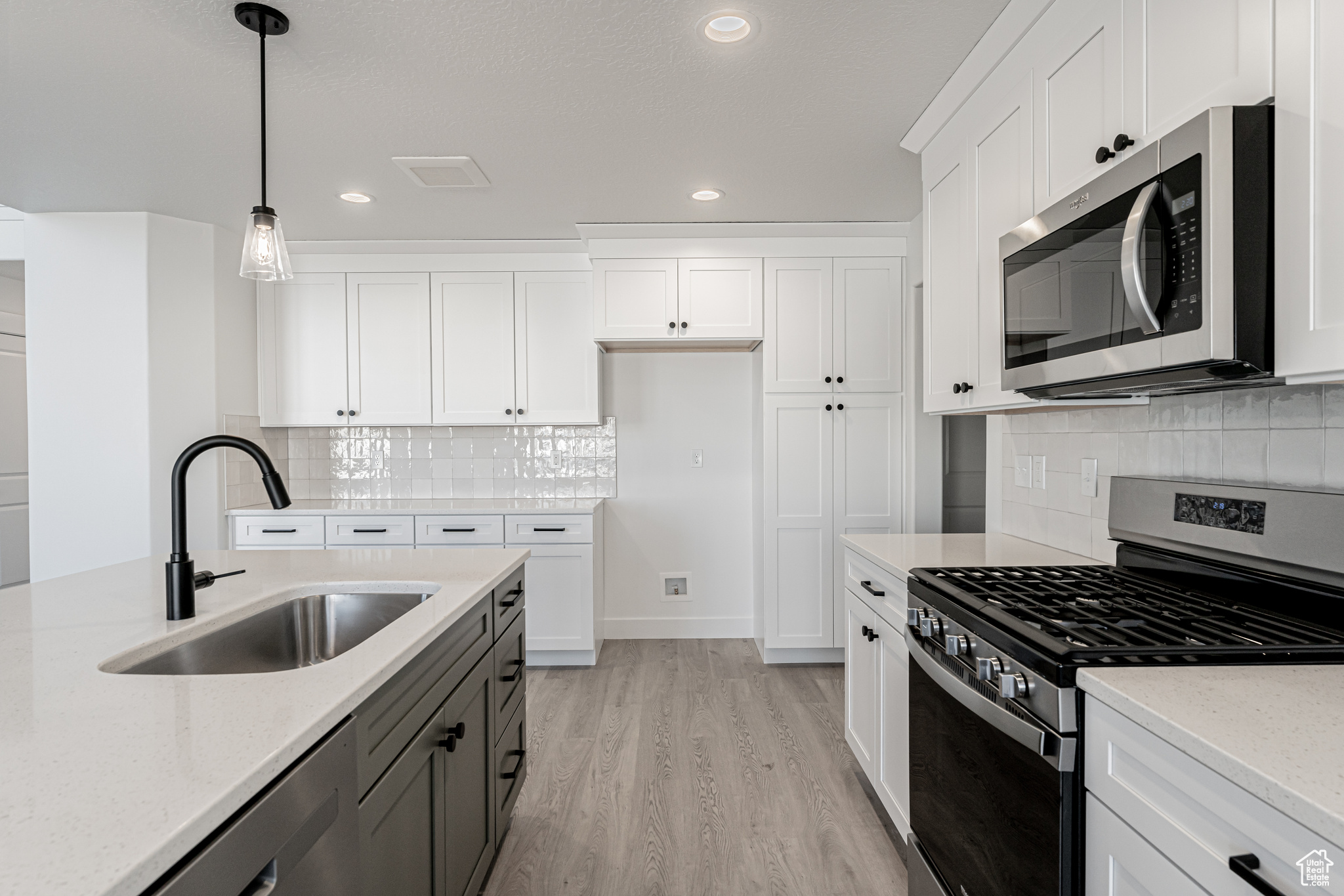 Kitchen featuring sink, white cabinetry, hanging light fixtures, stainless steel appliances, and light stone countertops