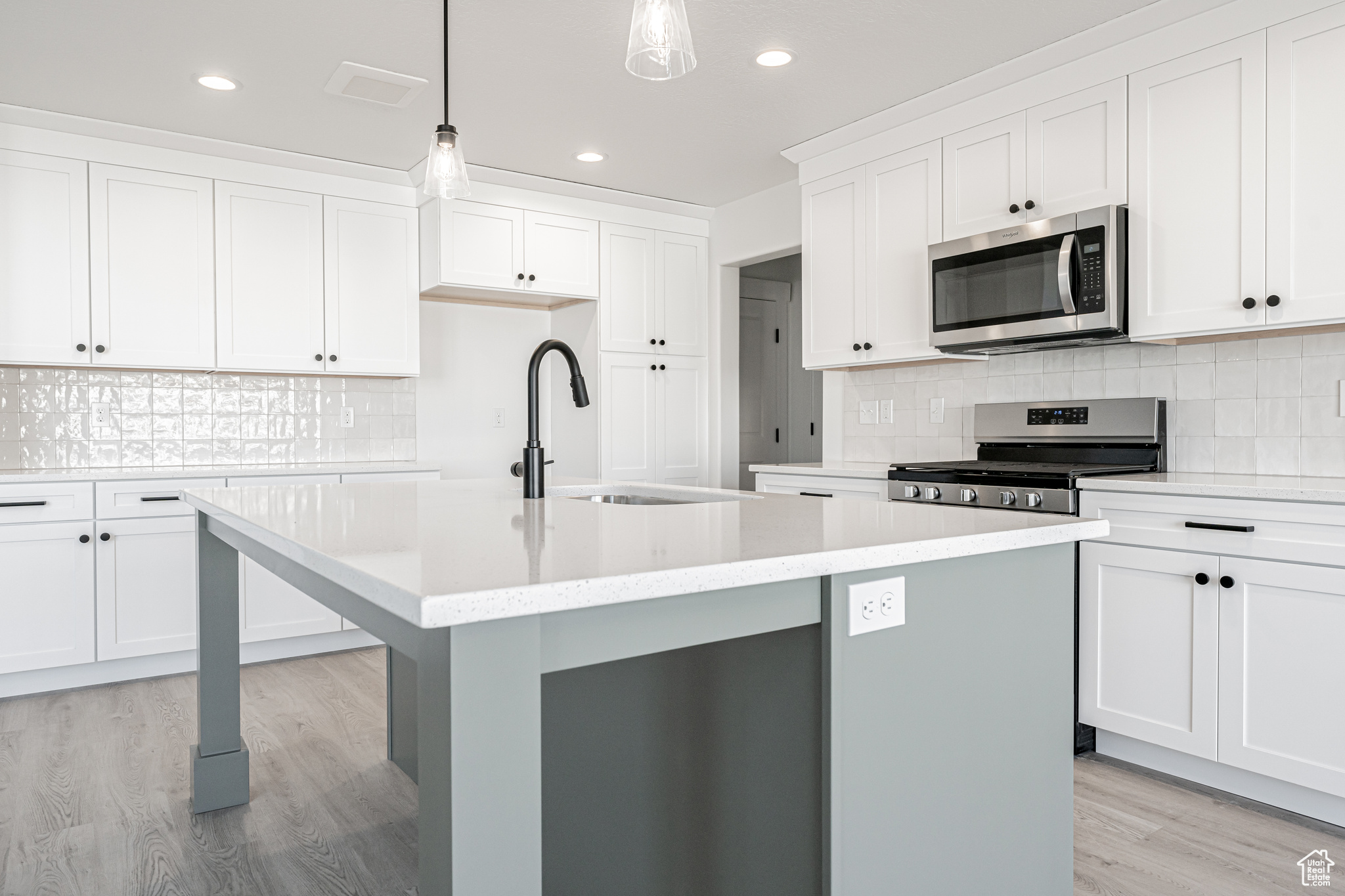 Kitchen featuring white cabinetry, stainless steel appliances, light hardwood / wood-style floors, an island with sink, and decorative light fixtures