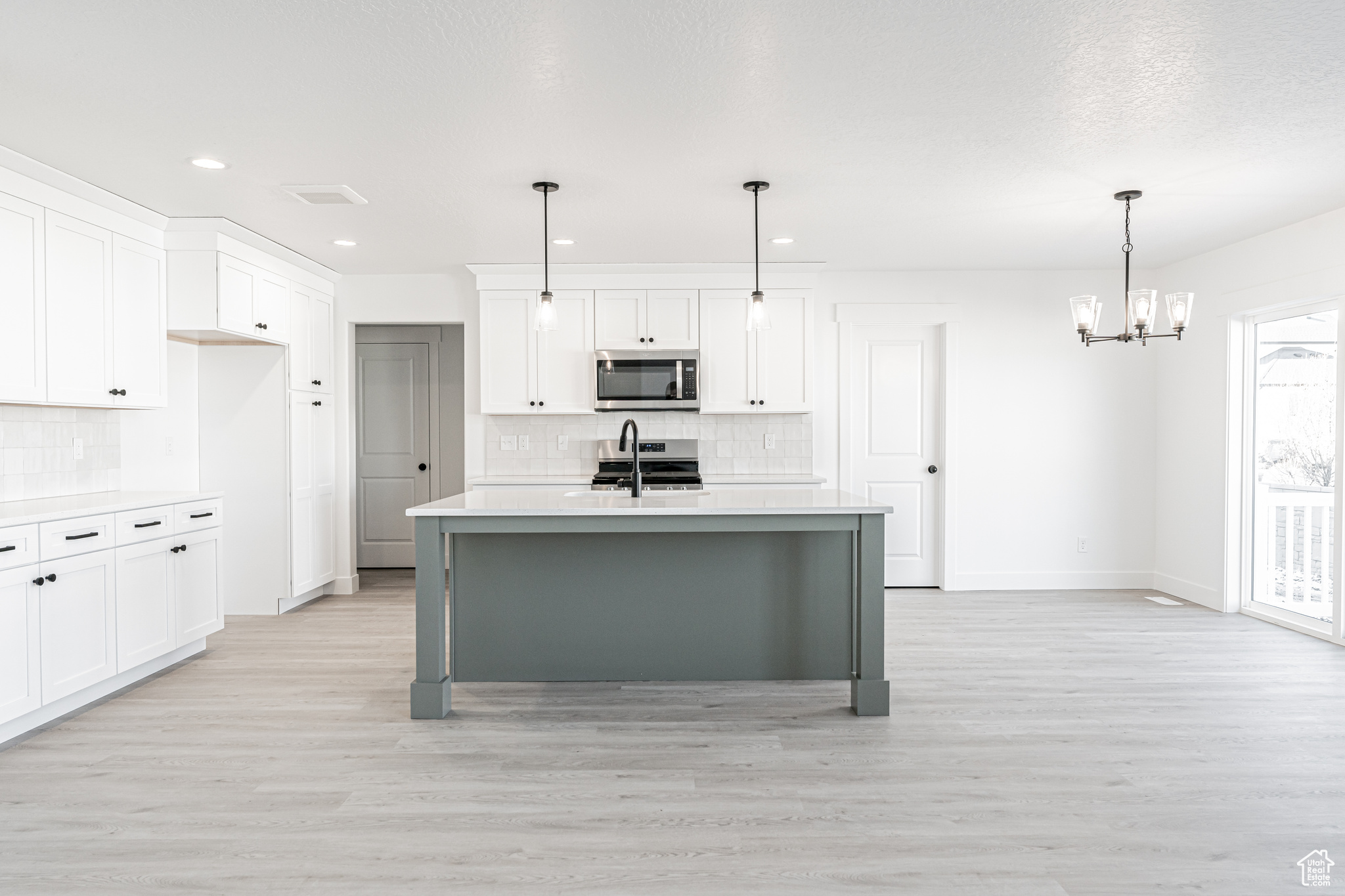 Kitchen featuring light hardwood / wood-style flooring, appliances with stainless steel finishes, white cabinetry, an island with sink, and decorative light fixtures