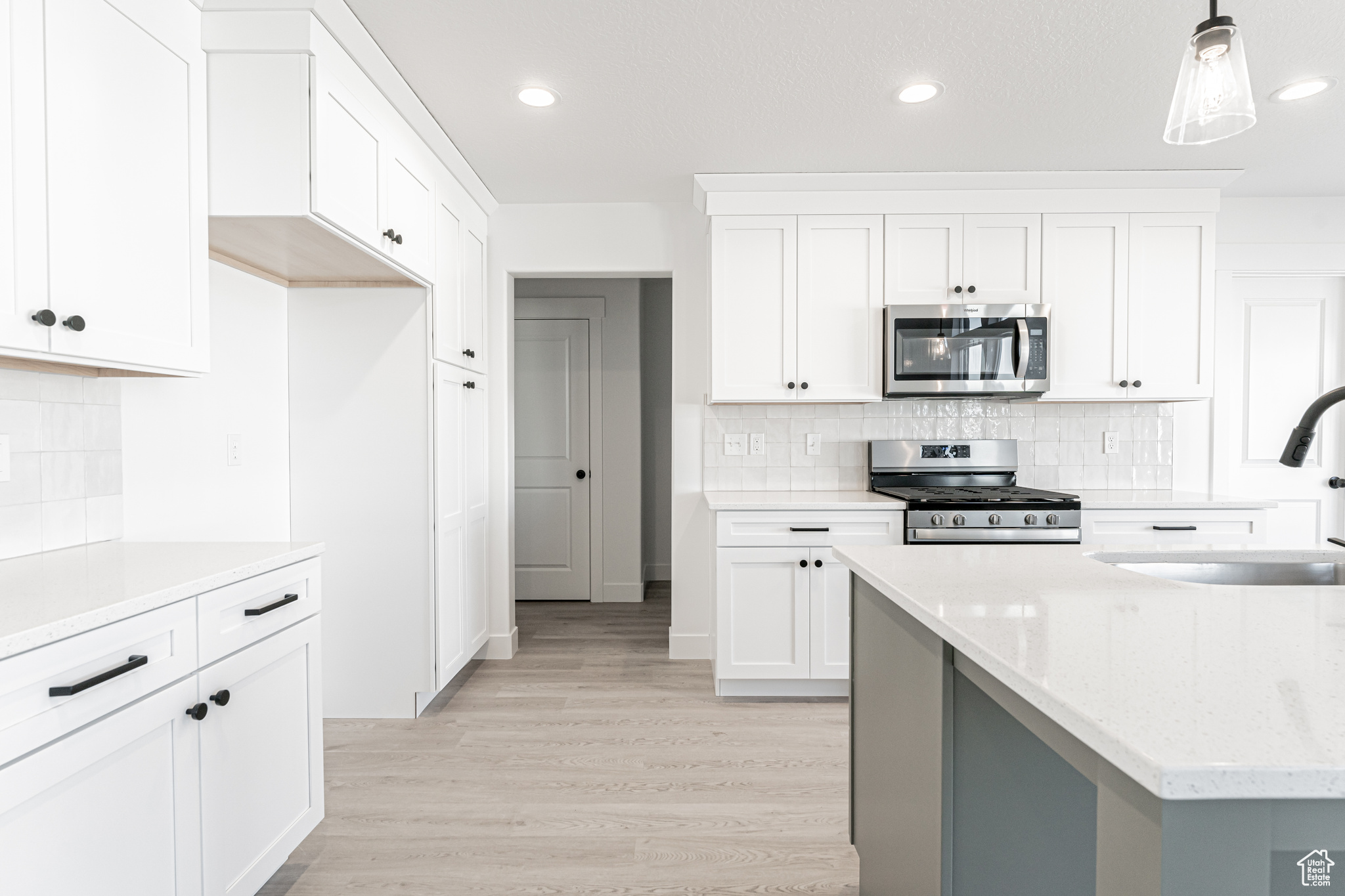 Kitchen with sink, white cabinetry, pendant lighting, stainless steel appliances, and light stone countertops