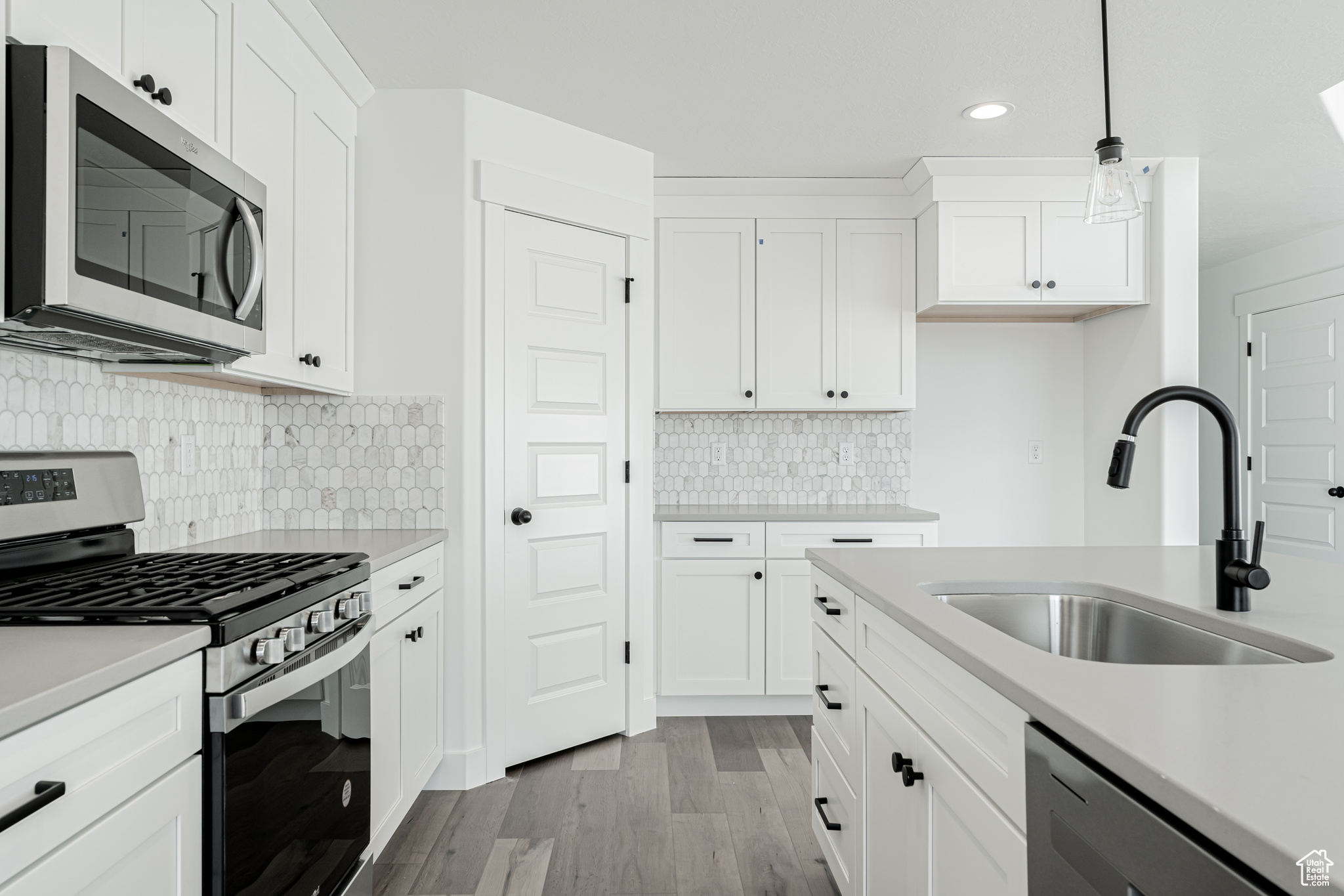 Kitchen featuring appliances with stainless steel finishes, pendant lighting, white cabinetry, and sink