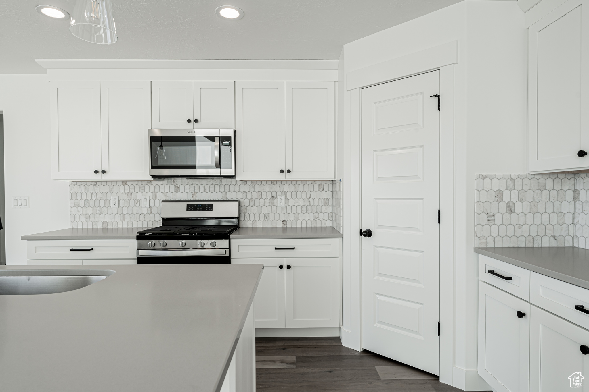 Kitchen with dark wood-type flooring, decorative light fixtures, decorative backsplash, white cabinets, and appliances with stainless steel finishes