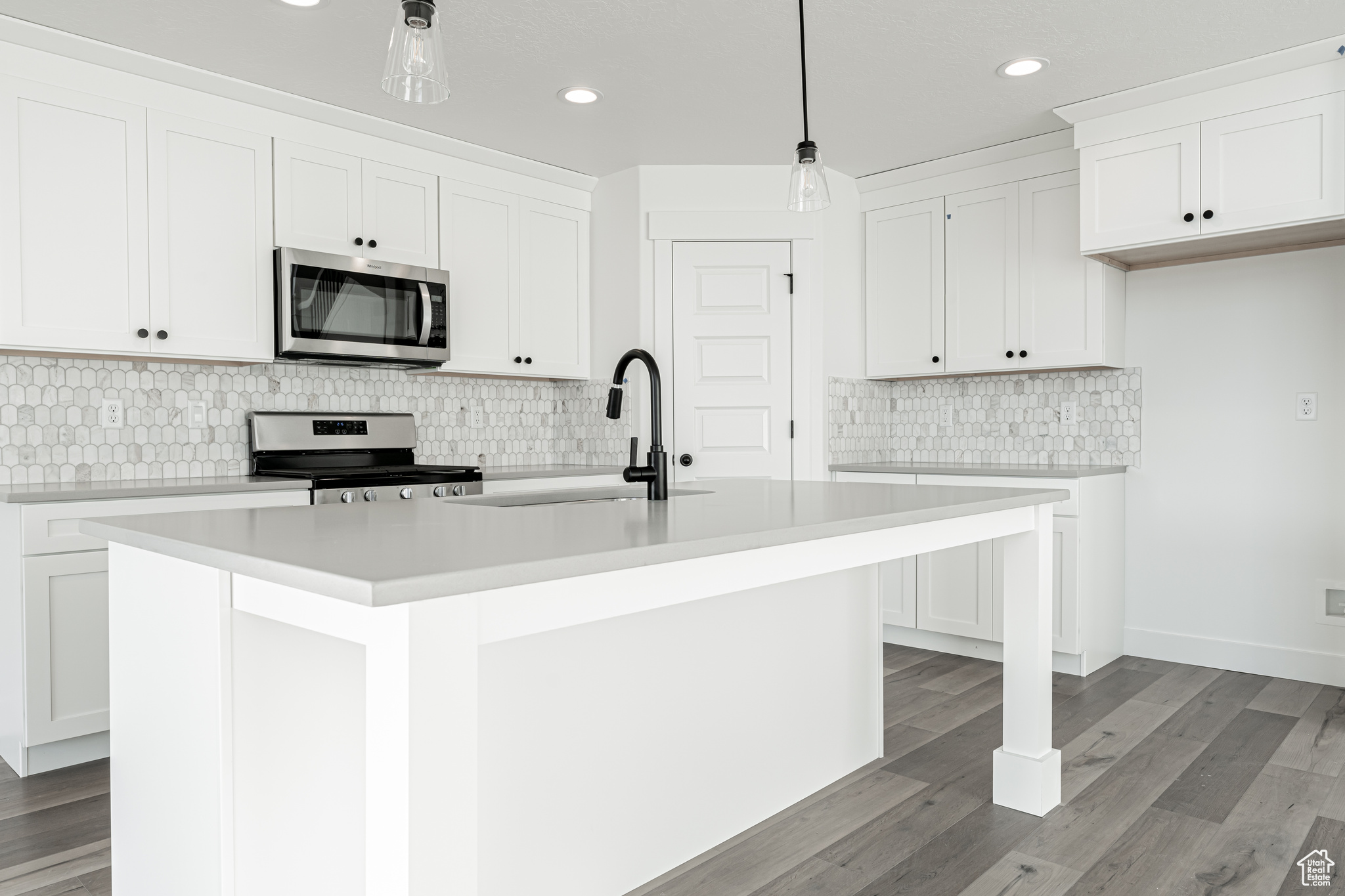 Kitchen with stainless steel appliances, an island with sink, hanging light fixtures, sink, and white cabinetry