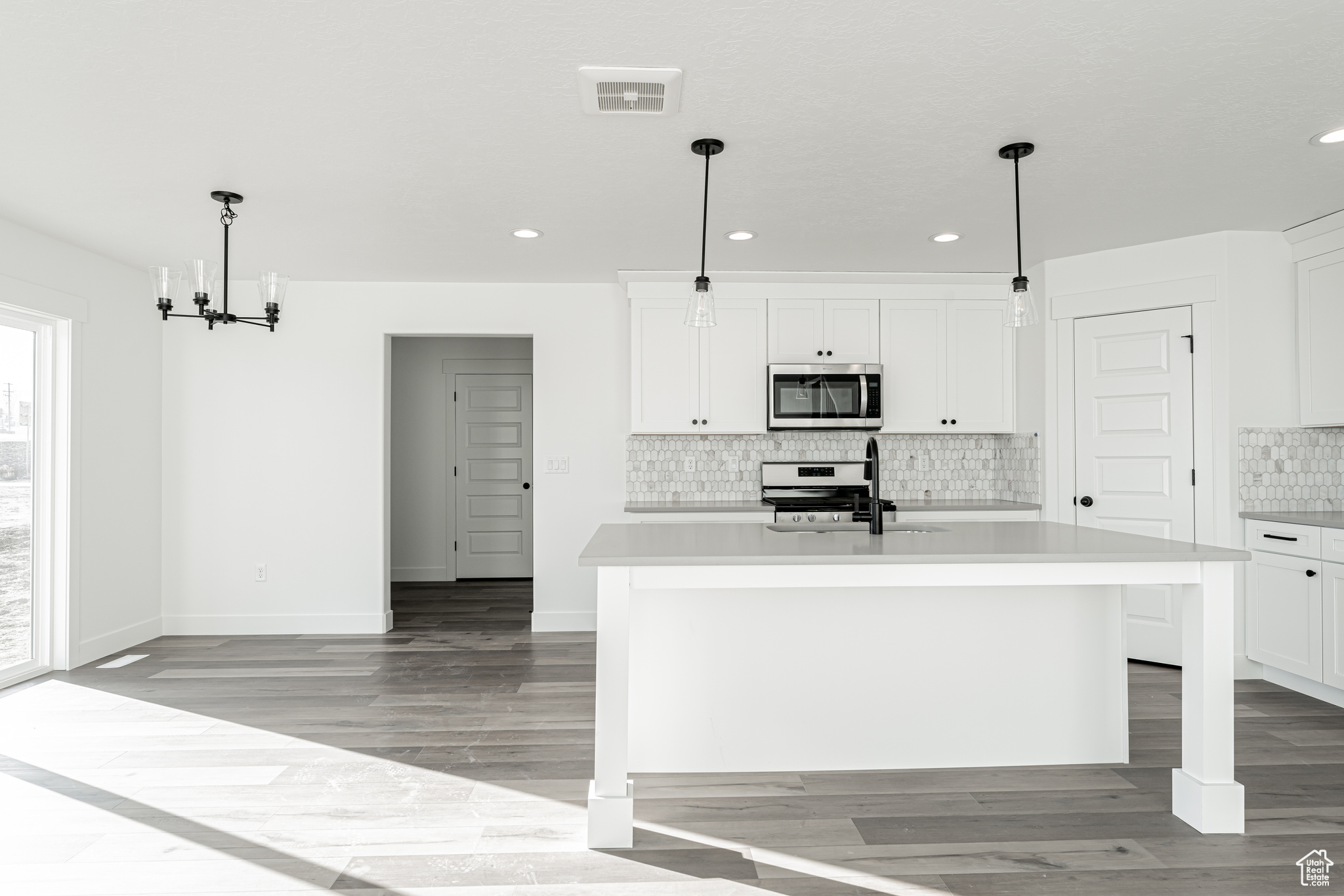 Kitchen with stainless steel appliances, a center island with sink, white cabinets, and decorative light fixtures