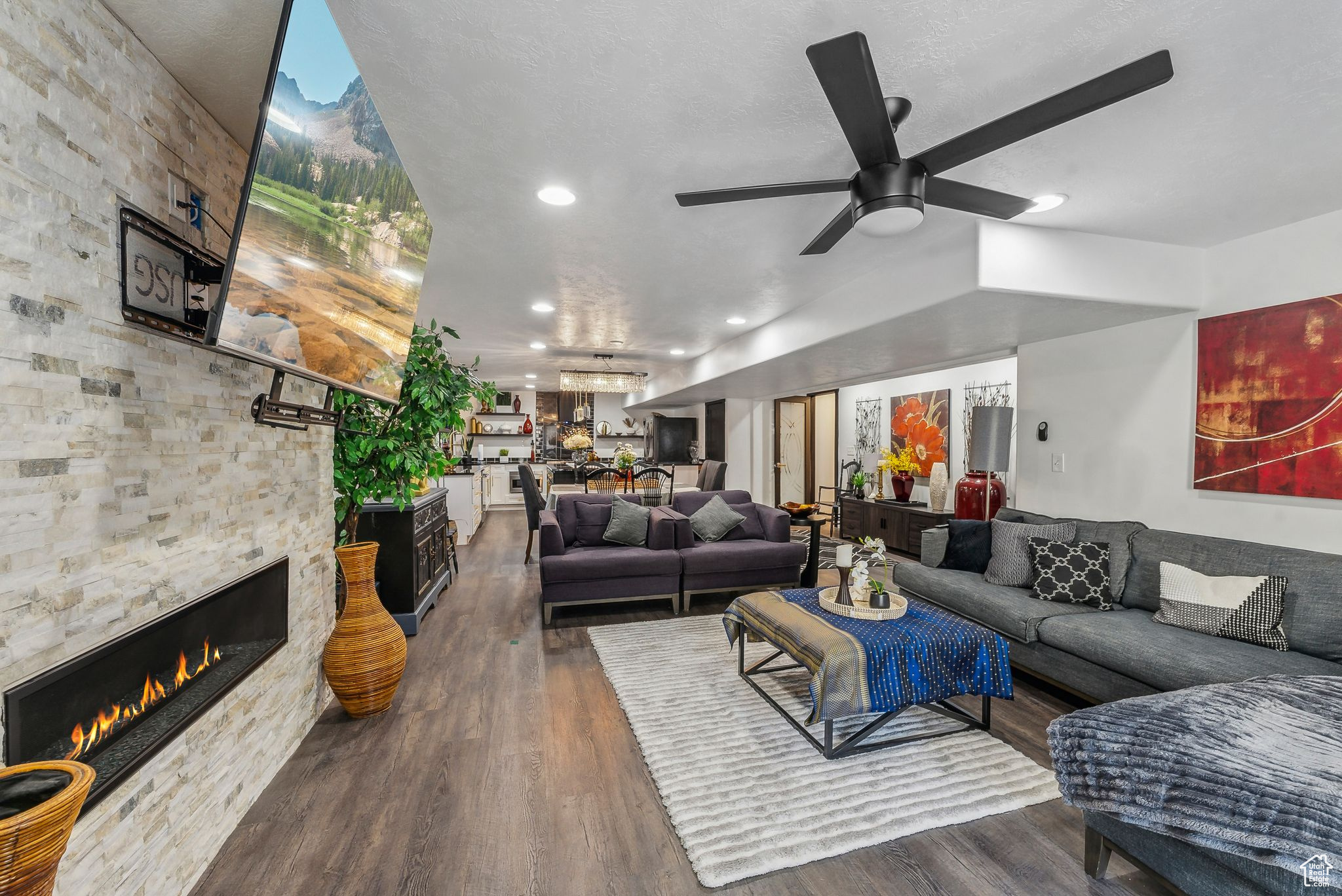 Living room featuring a stone fireplace, dark hardwood / wood-style flooring, a textured ceiling, and ceiling fan