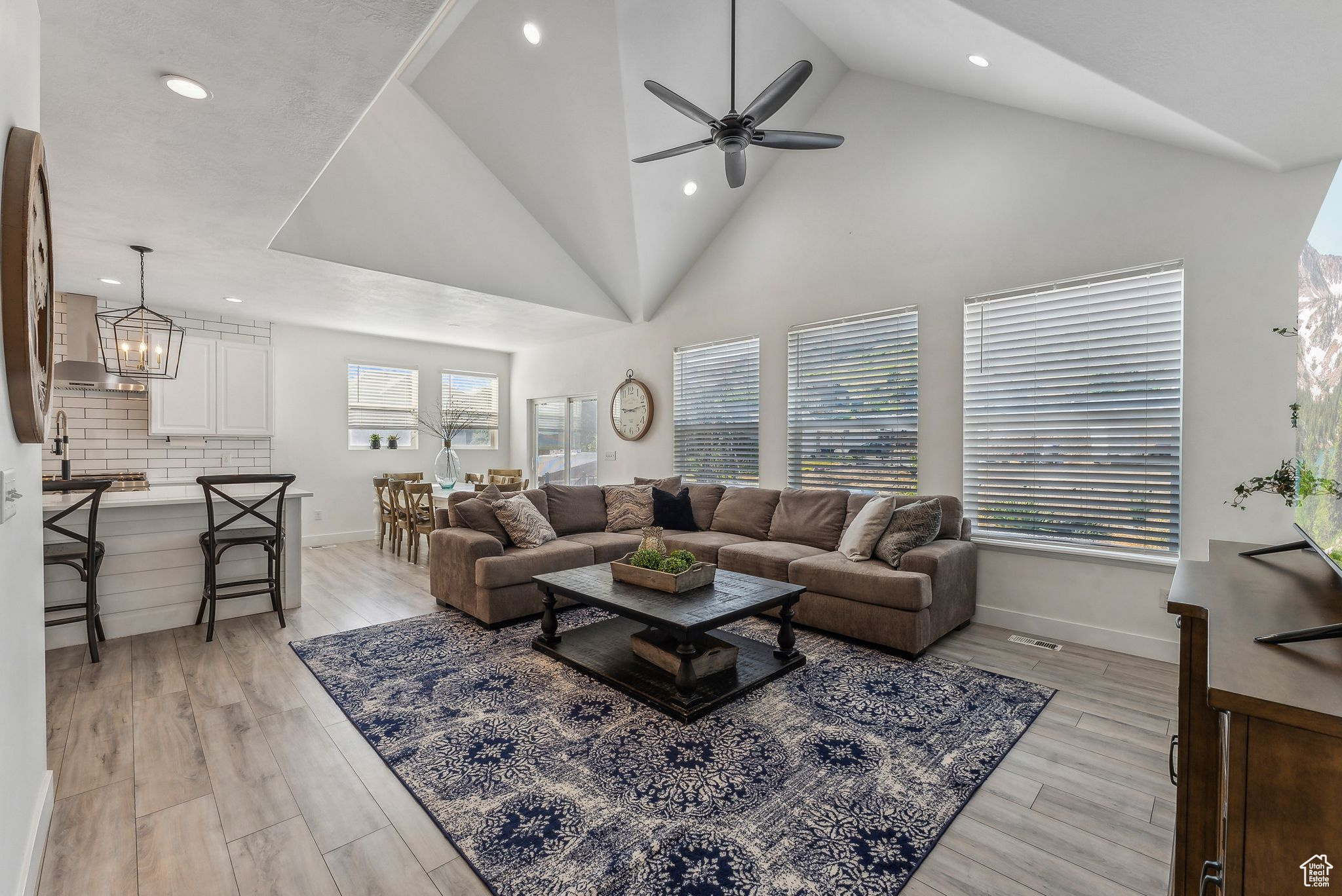 Living room featuring high vaulted ceiling, light wood-type flooring, and ceiling fan with notable chandelier