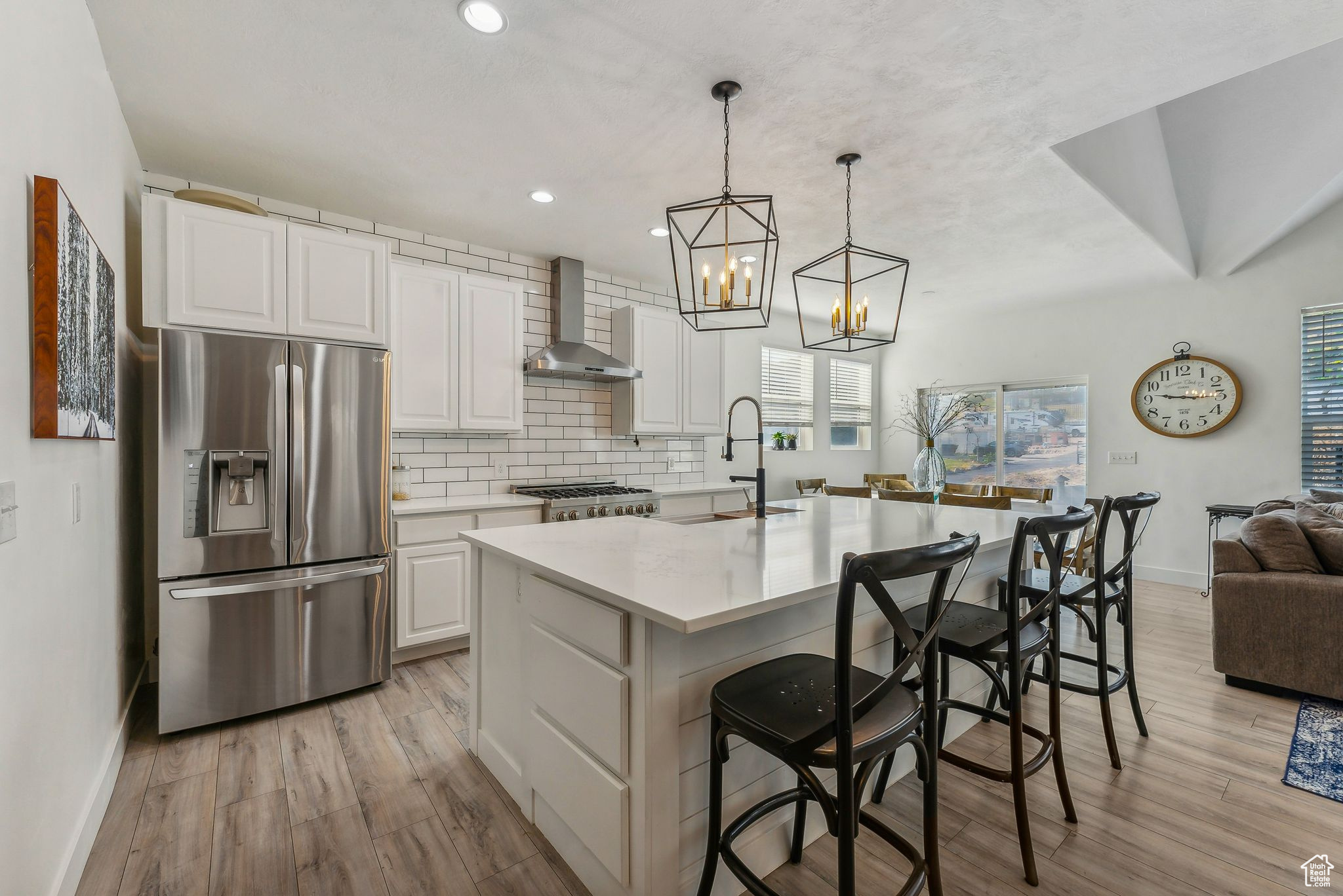 Kitchen with a center island with sink, light hardwood / wood-style floors, wall chimney exhaust hood, and stainless steel refrigerator with ice dispenser