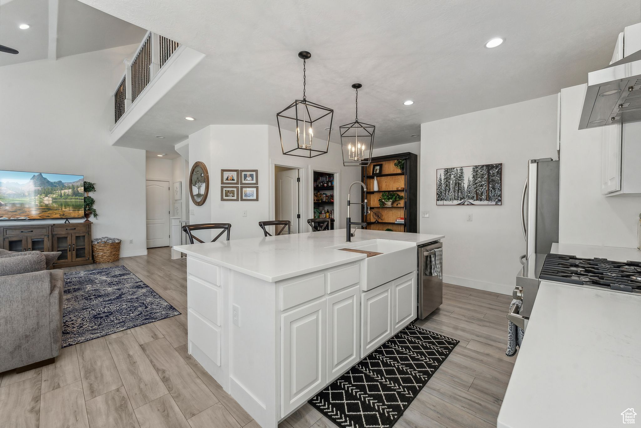 Kitchen with decorative light fixtures, white cabinets, light wood-type flooring, a center island with sink, and appliances with stainless steel finishes