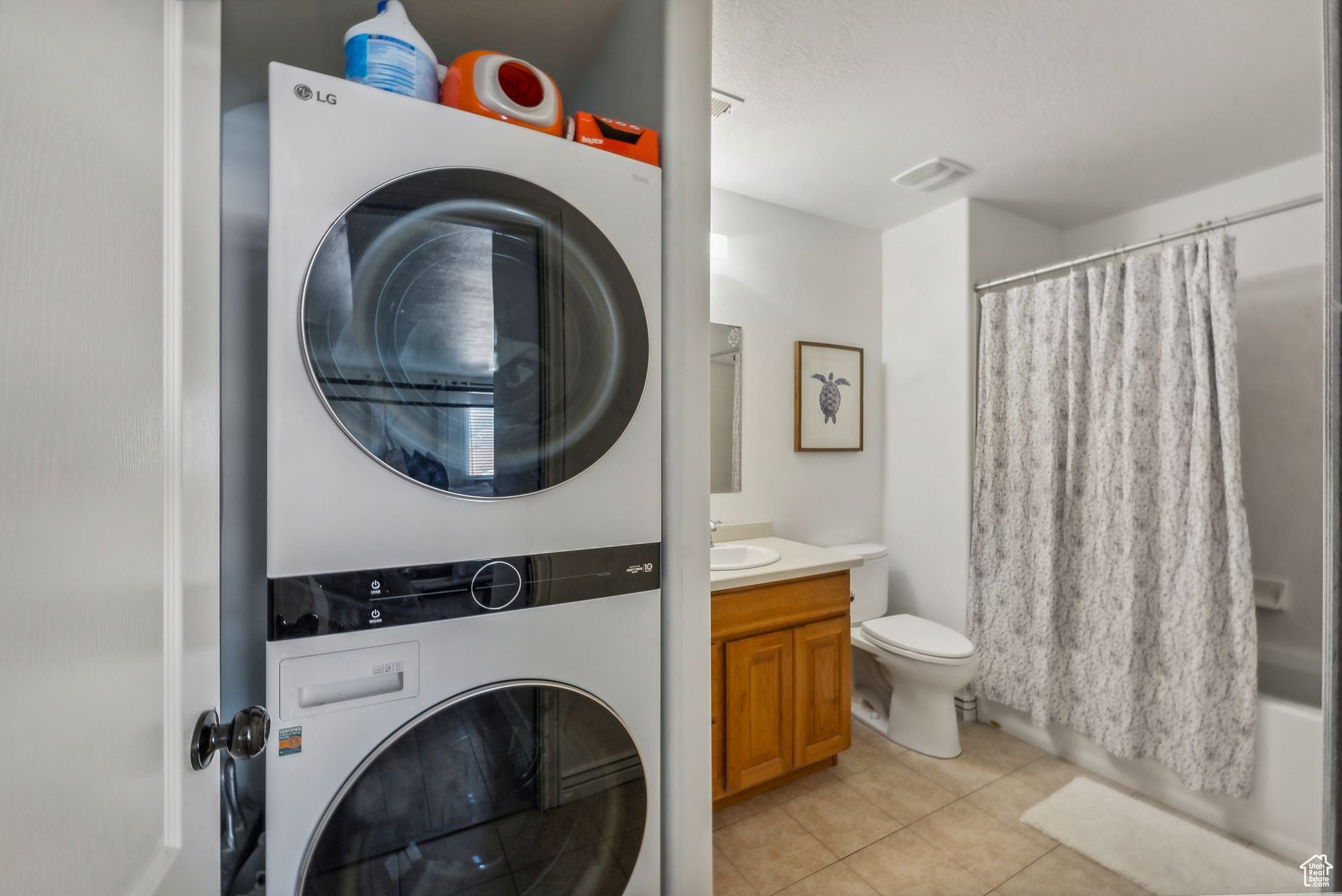 Laundry room with stacked washer and dryer, sink, and light tile patterned floors