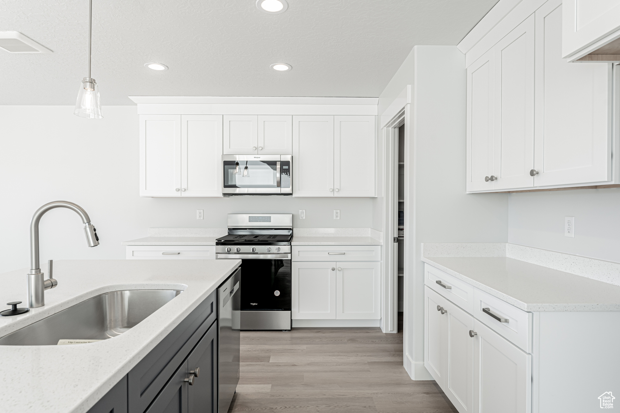 Kitchen featuring appliances with stainless steel finishes, sink, white cabinets, and decorative light fixtures