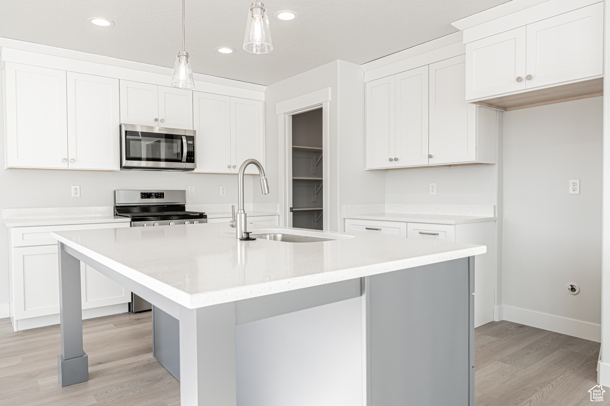 Kitchen featuring stainless steel appliances, decorative light fixtures, a center island with sink, and white cabinets