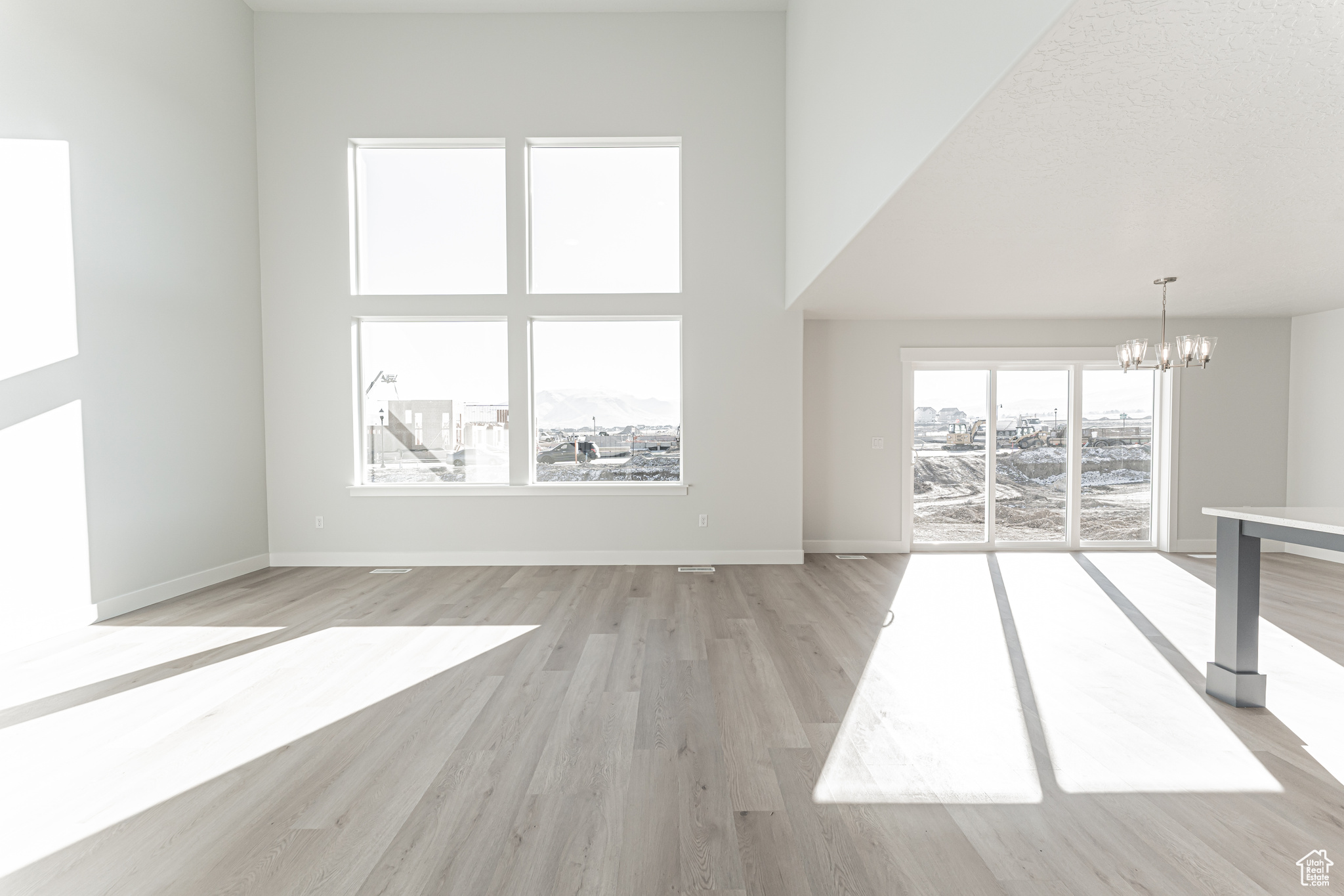 Unfurnished living room featuring an inviting chandelier, a towering ceiling, and light hardwood / wood-style flooring