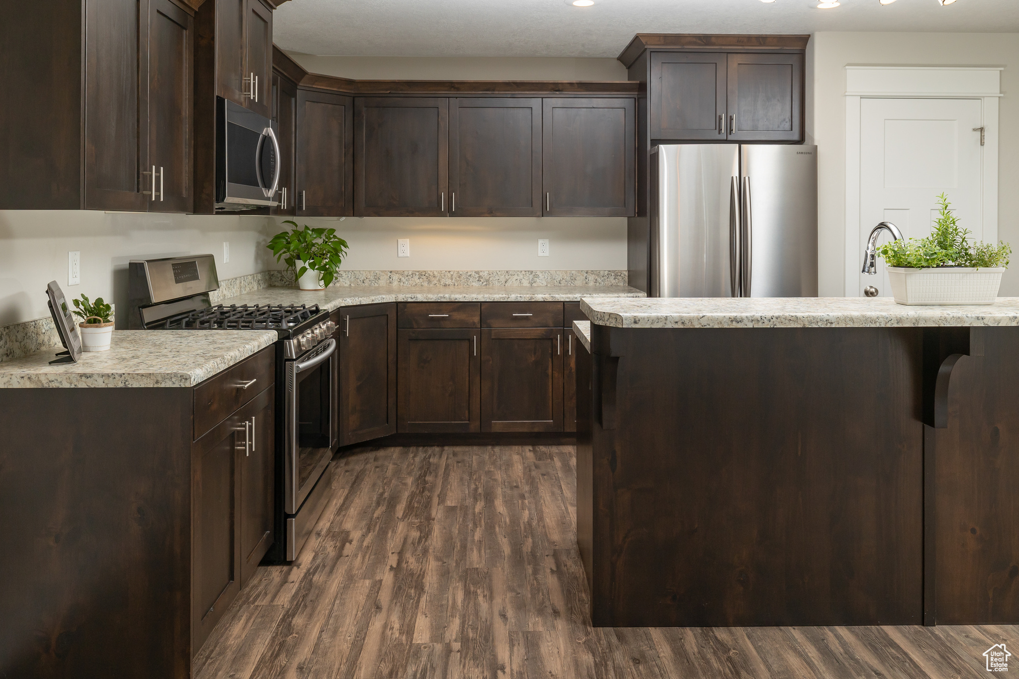 Kitchen featuring dark brown cabinets, light stone counters, dark hardwood / wood-style flooring, and appliances with stainless steel finishes