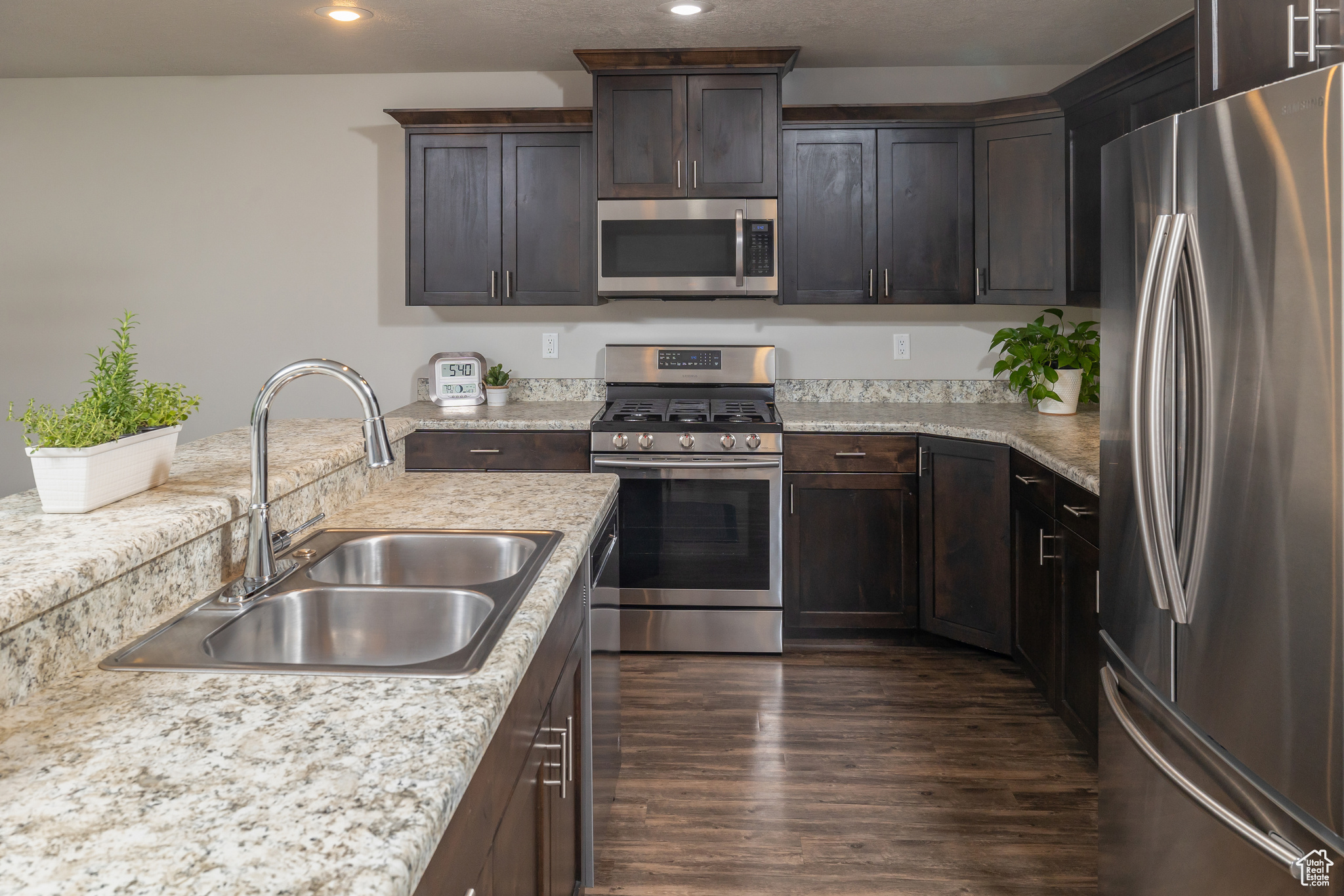 Kitchen featuring stainless steel appliances, sink, light stone counters, dark hardwood / wood-style floors, and dark brown cabinetry