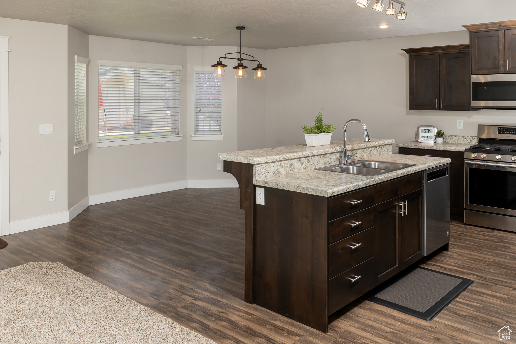 Kitchen featuring dark hardwood / wood-style floors, appliances with stainless steel finishes, sink, decorative light fixtures, and a center island with sink