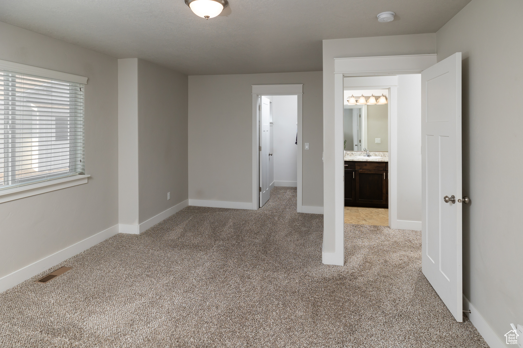 Unfurnished bedroom featuring ensuite bath, sink, and light carpet