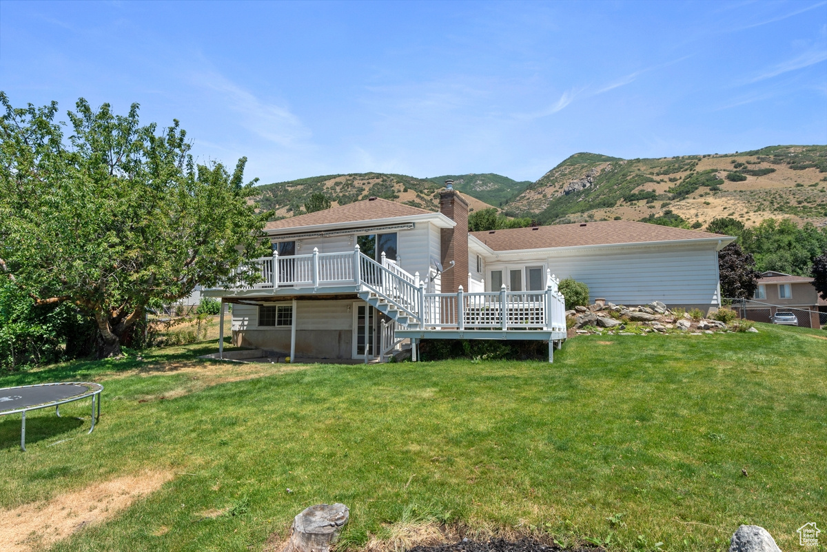 Rear view of property with a trampoline, a lawn, and a deck with mountain view