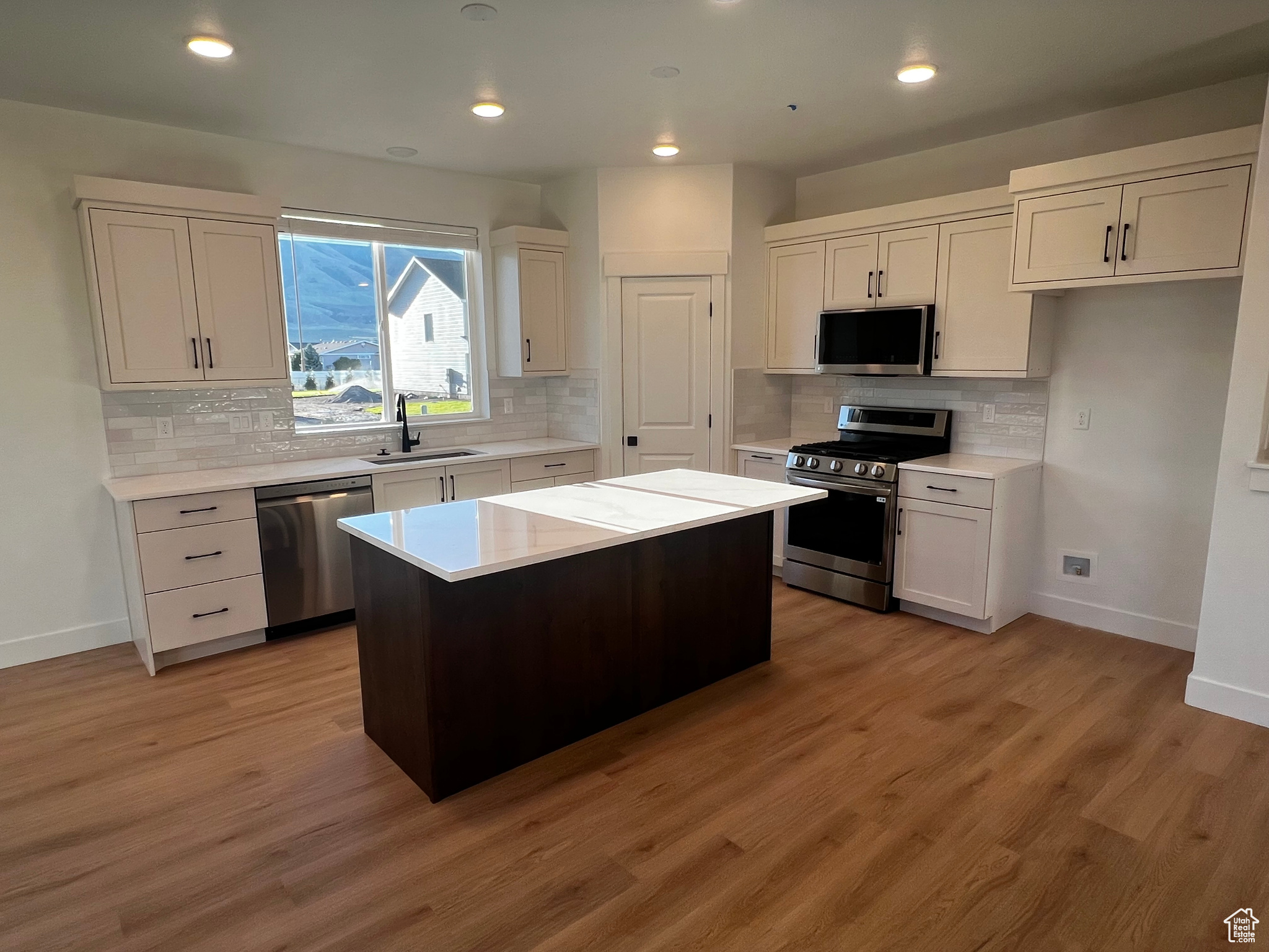 Kitchen with hardwood / wood-style flooring, decorative backsplash, a kitchen island, white cabinetry, and stainless steel appliances