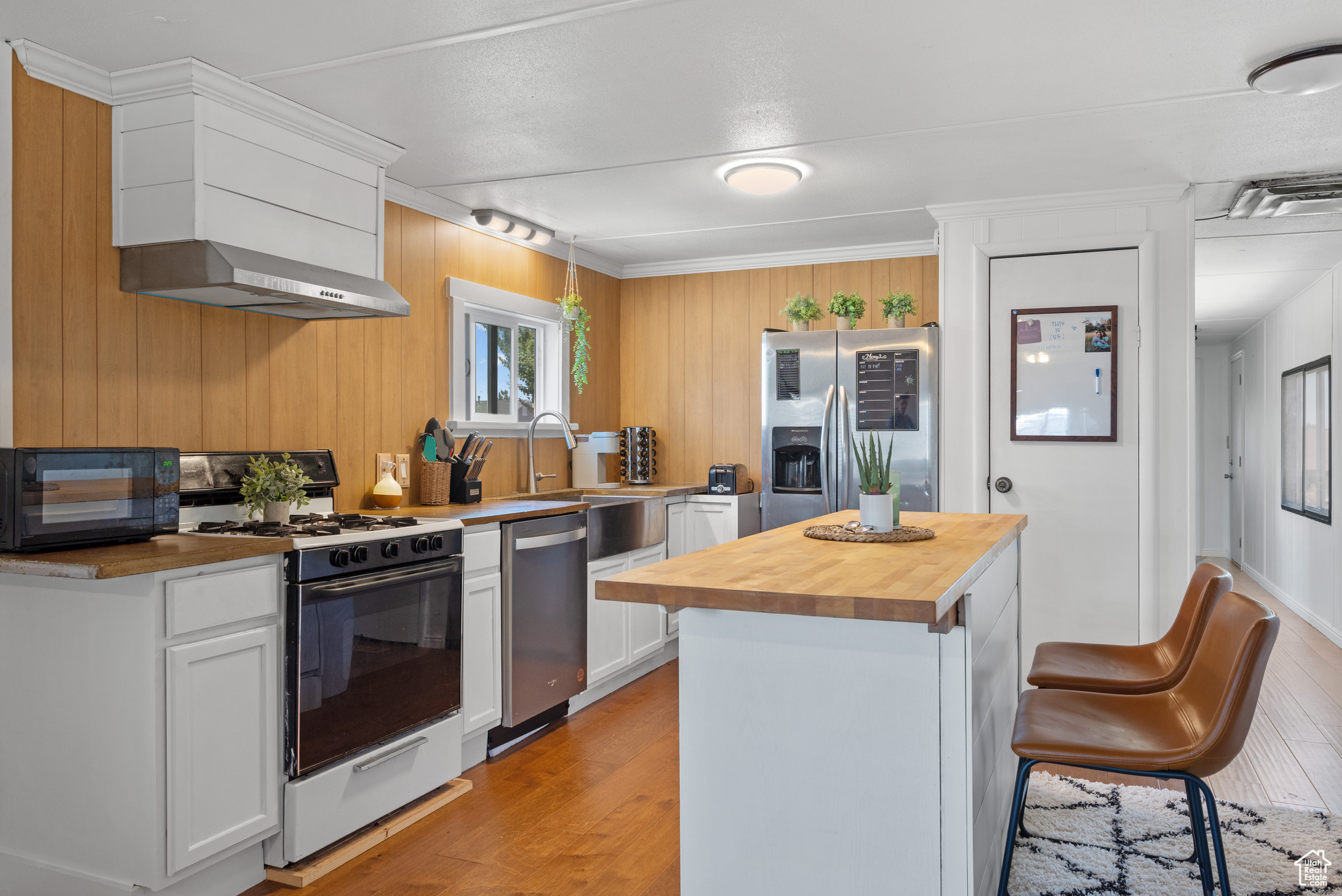 Kitchen featuring white cabinetry, light hardwood / wood-style flooring, a kitchen island, stainless steel appliances, and butcher block countertops