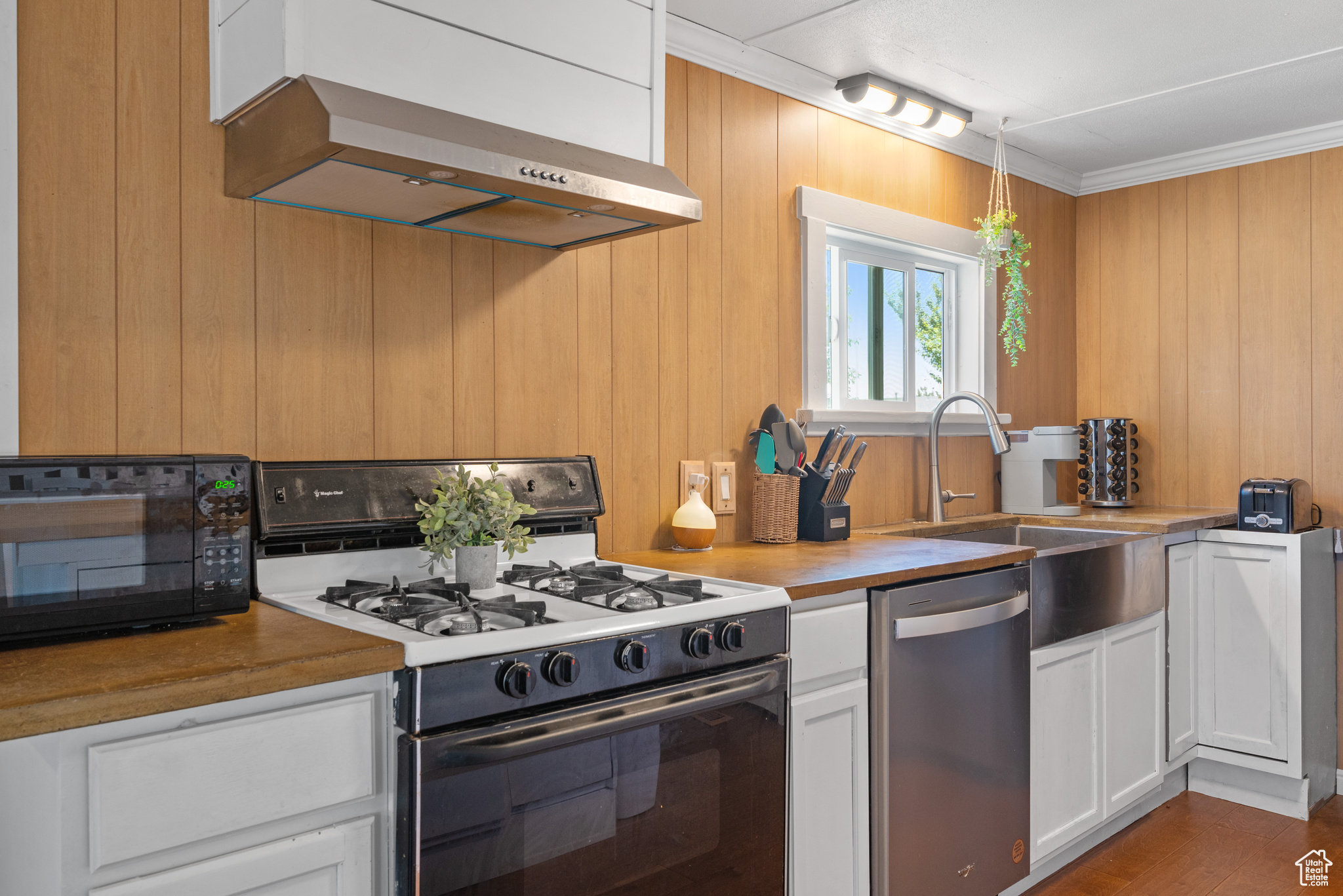 Kitchen featuring gas range gas stove, wall chimney range hood, white cabinetry, and dishwasher