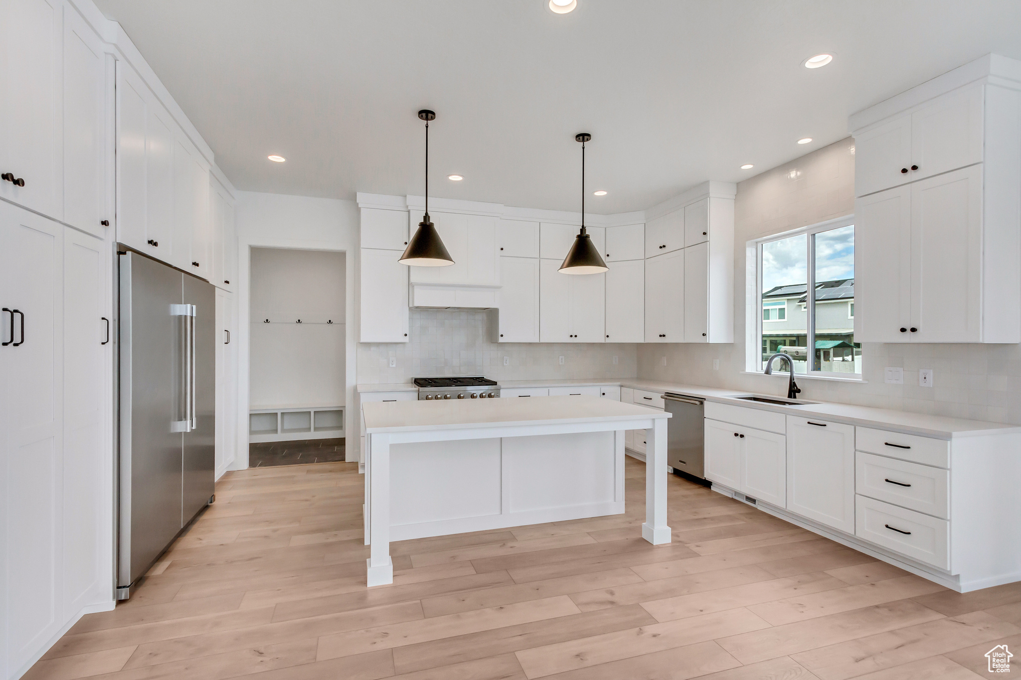 Kitchen featuring light wood-type flooring, backsplash, stainless steel appliances, and hanging light fixtures