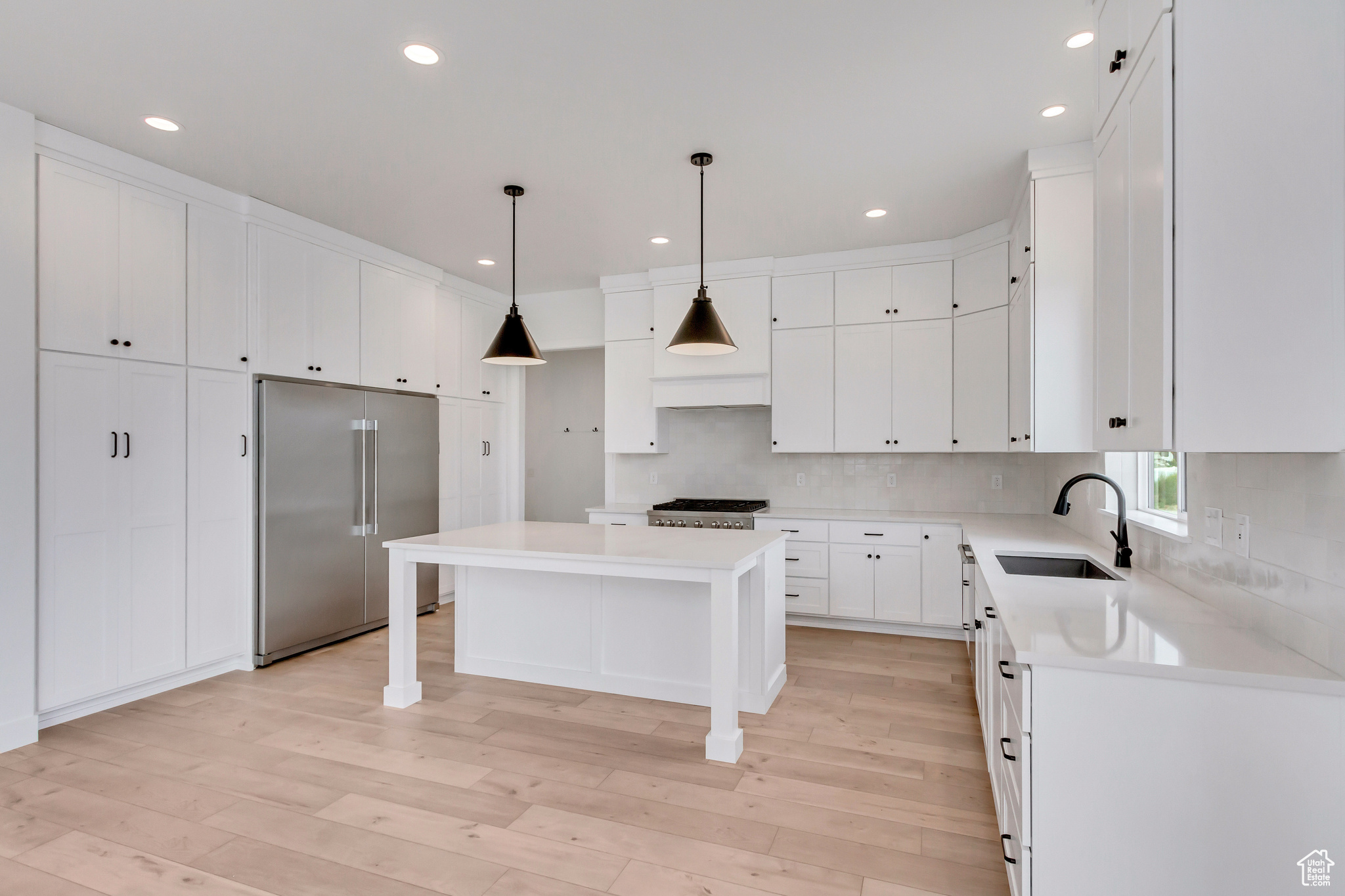 Kitchen with light hardwood / wood-style flooring, backsplash, stainless steel built in fridge, sink, and a center island