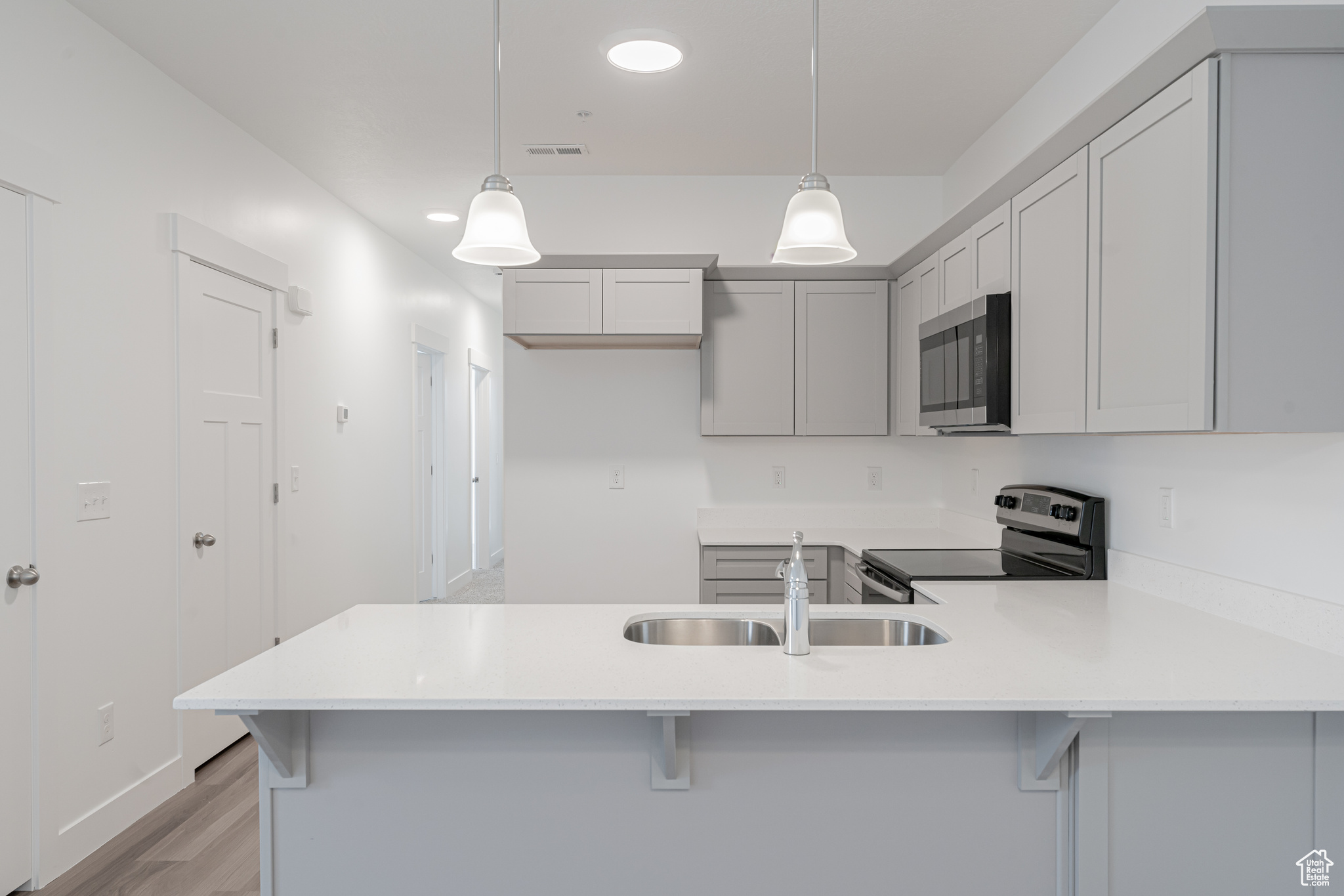 Kitchen with appliances with stainless steel finishes, light hardwood / wood-style flooring, kitchen peninsula, and hanging light fixtures