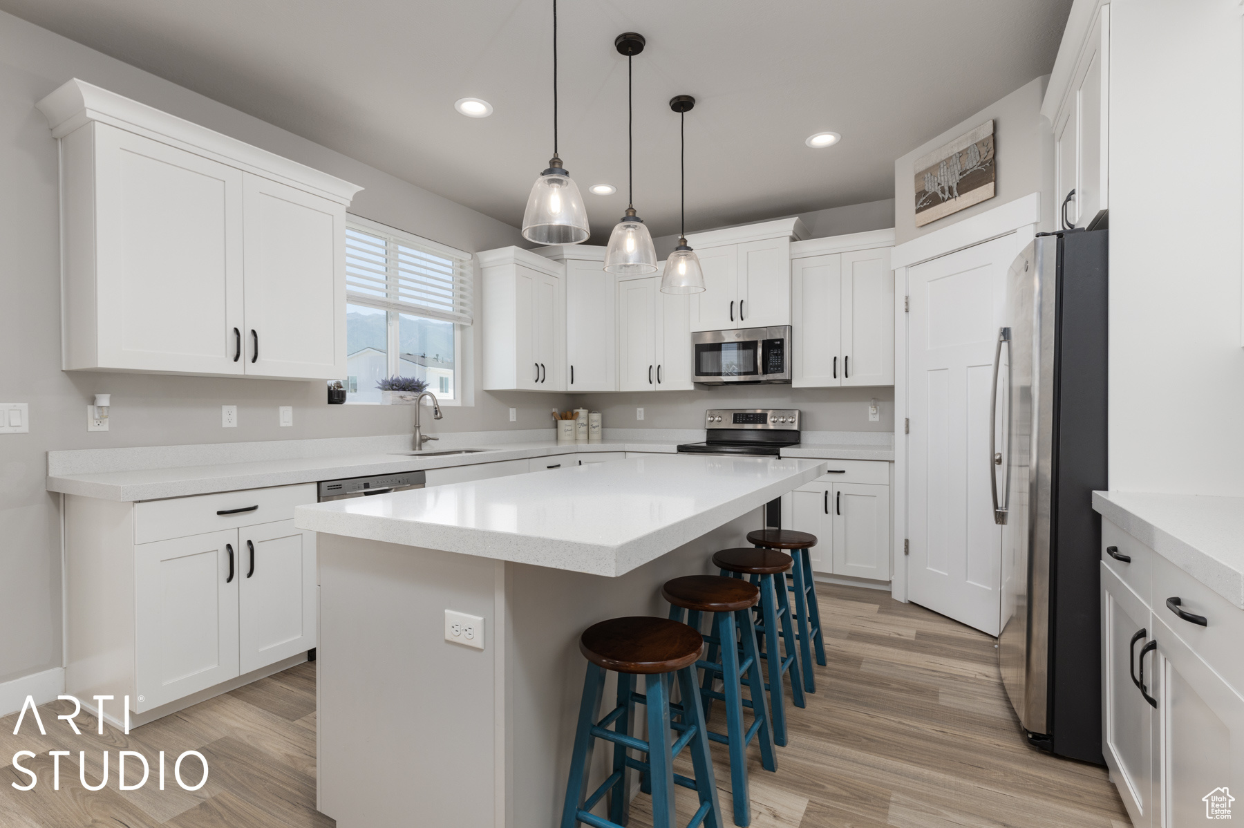 Kitchen with sink, appliances with stainless steel finishes, white cabinetry, and light wood-type flooring