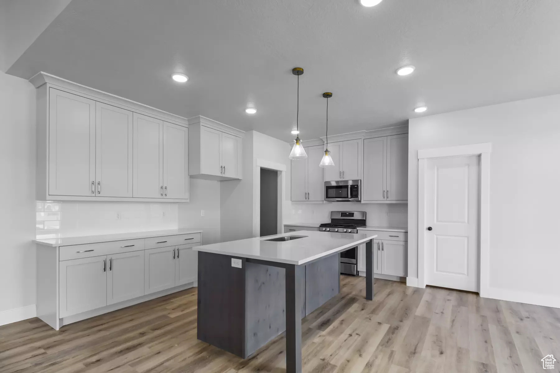 Kitchen featuring appliances with stainless steel finishes, hanging light fixtures, light hardwood / wood-style floors, a kitchen island, and decorative backsplash