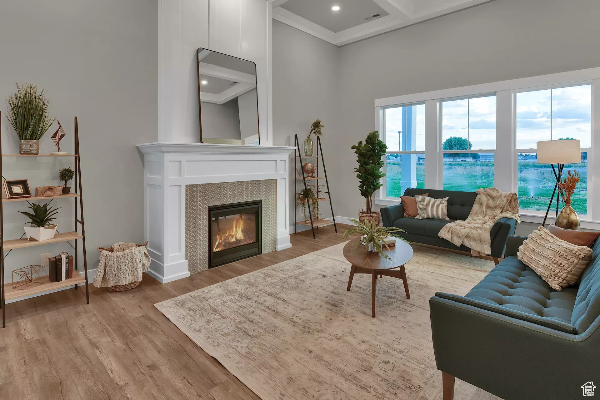 Living room featuring wood-type flooring, crown molding, coffered ceiling, a tiled fireplace, and a towering ceiling