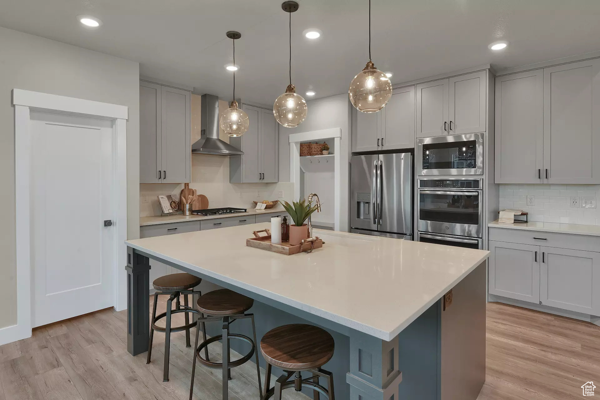 Kitchen with light hardwood / wood-style flooring, a center island, stainless steel appliances, wall chimney exhaust hood, and decorative backsplash