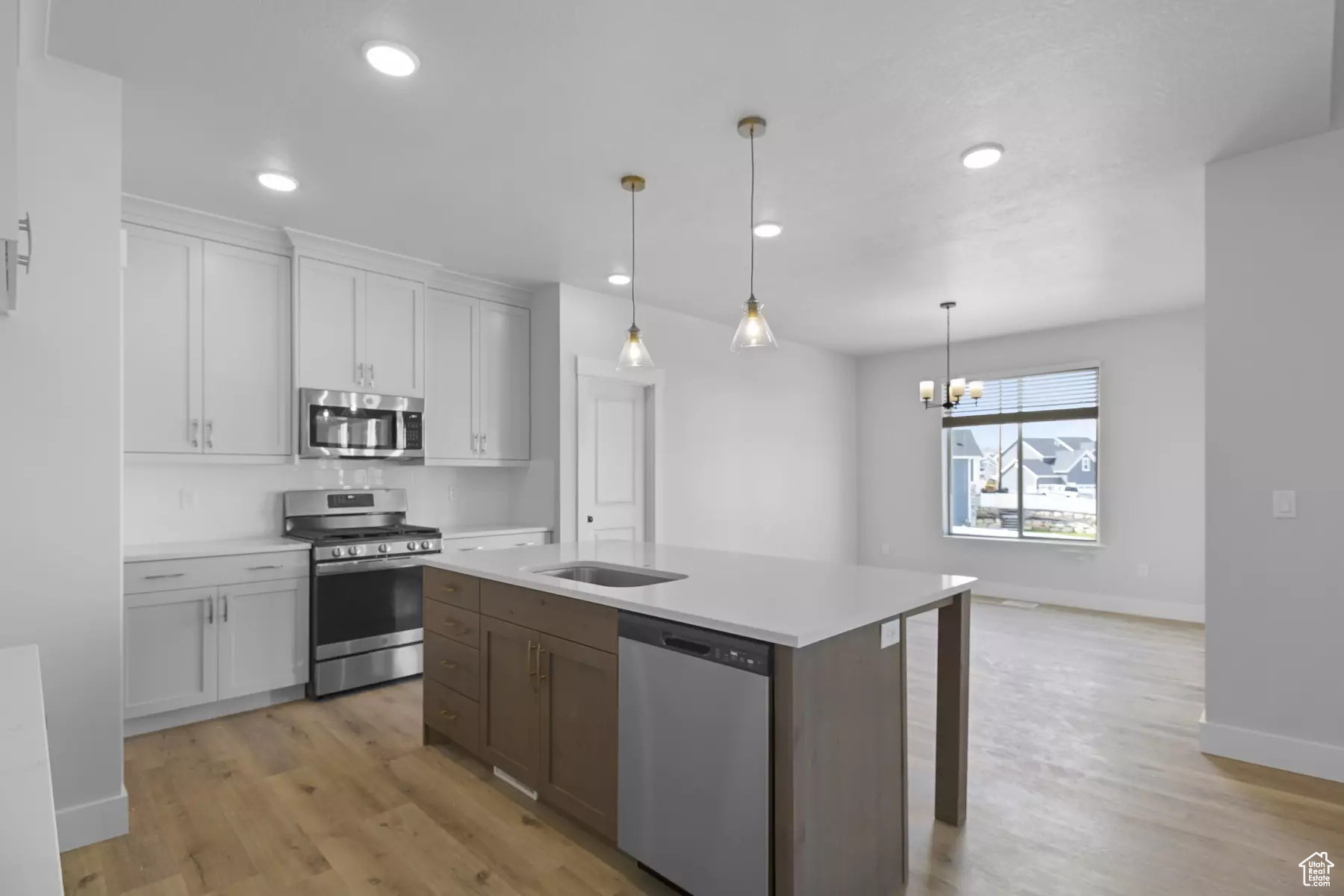 Kitchen featuring stainless steel appliances, an inviting chandelier, hanging light fixtures, light hardwood / wood-style floors, and a kitchen island with sink