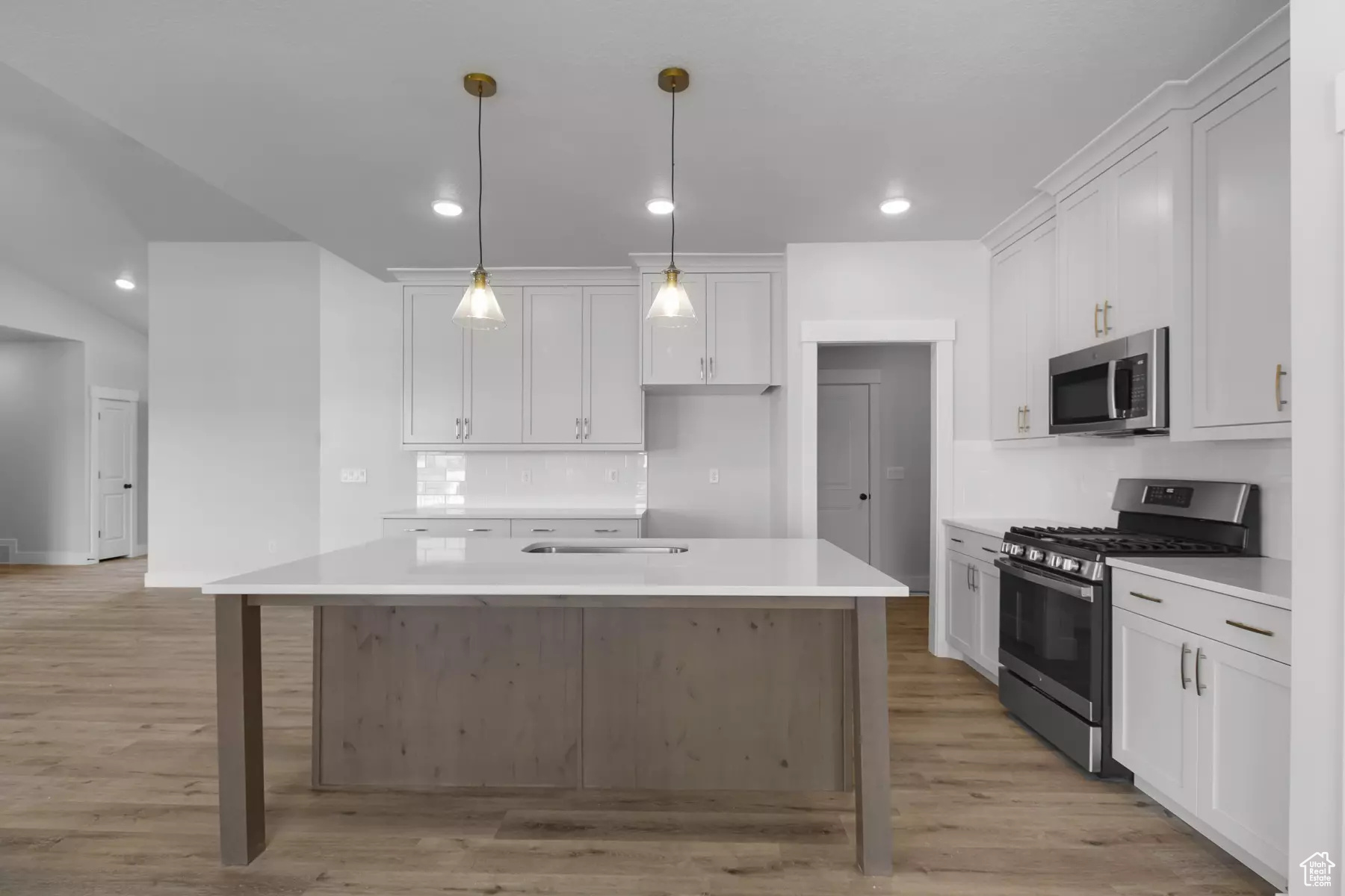 Kitchen with a kitchen island with sink, light hardwood / wood-style flooring, appliances with stainless steel finishes, and white cabinets