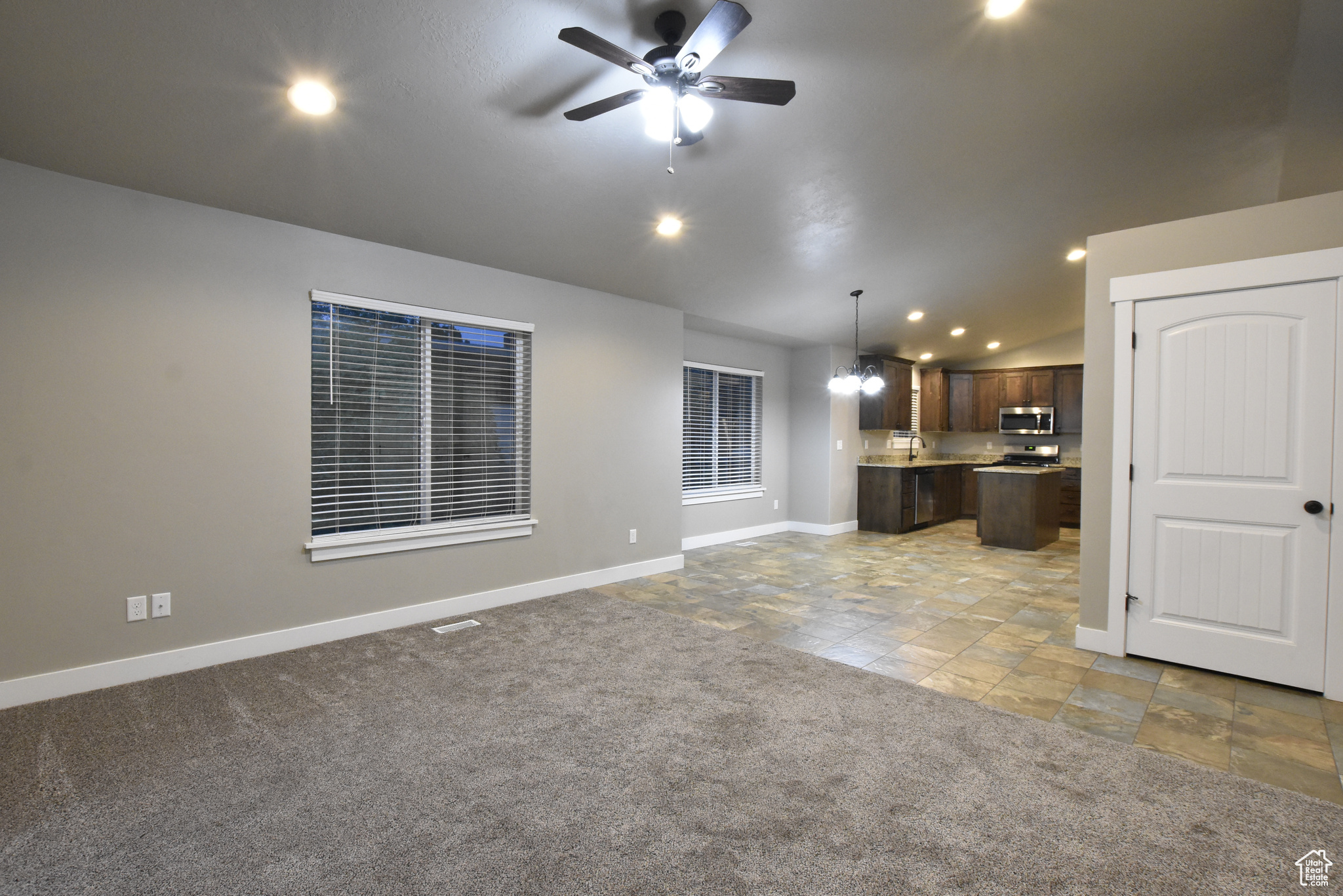 Unfurnished living room with light carpet, ceiling fan with notable chandelier, and lofted ceiling