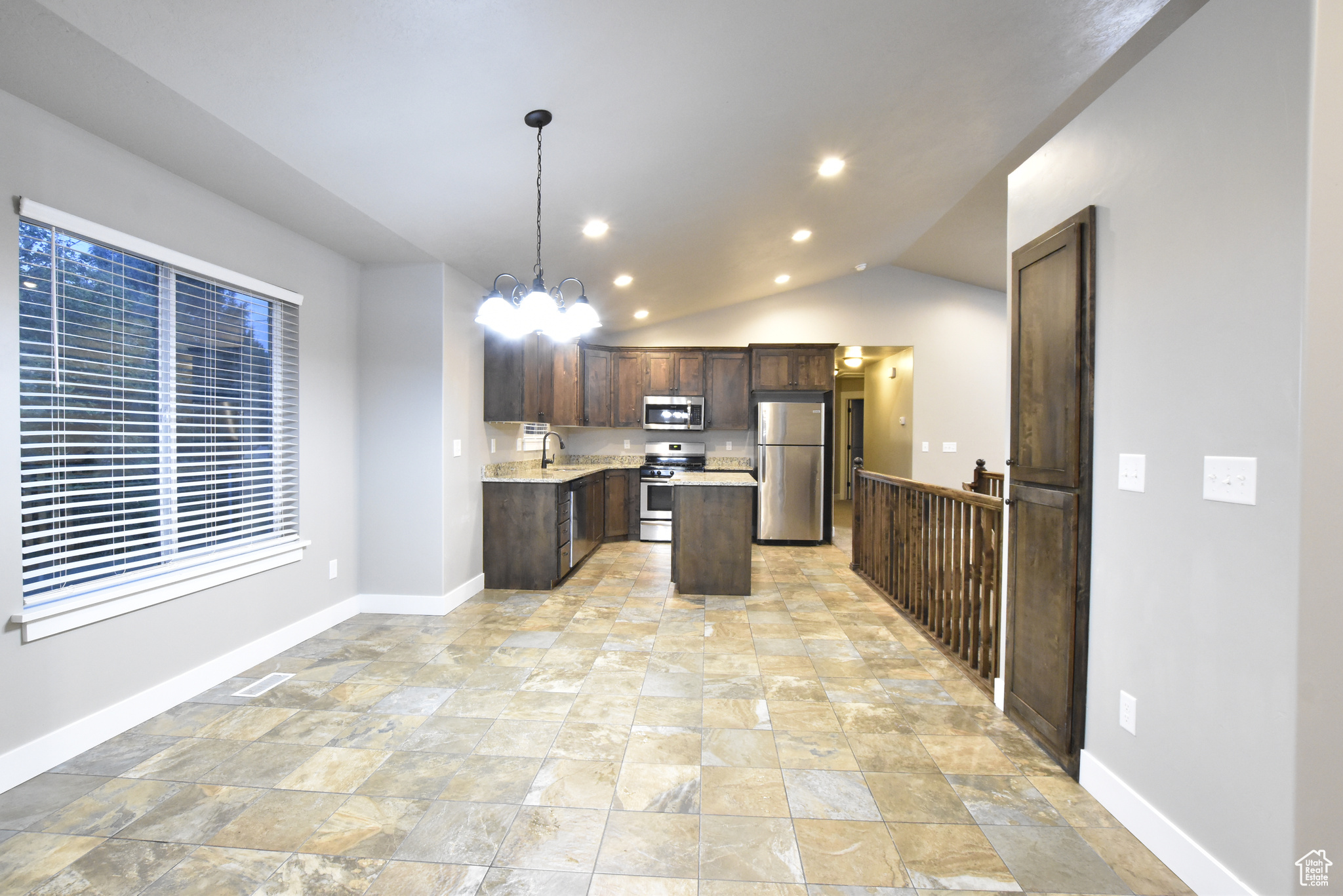 Kitchen featuring stainless steel appliances, pendant lighting, a center island, lofted ceiling, and light tile patterned floors