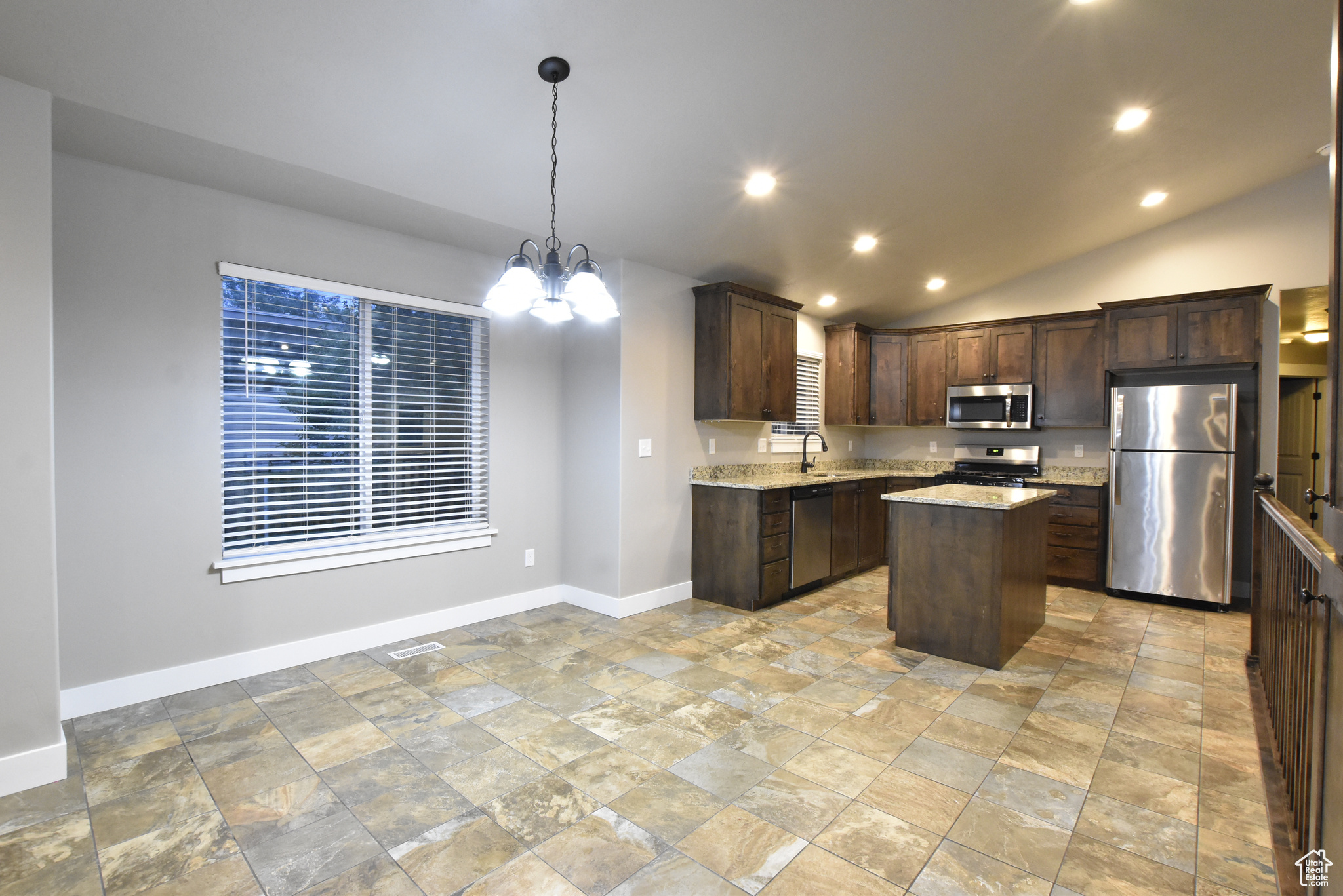 Kitchen featuring light tile patterned flooring, a kitchen island, stainless steel appliances, hanging light fixtures, and vaulted ceiling